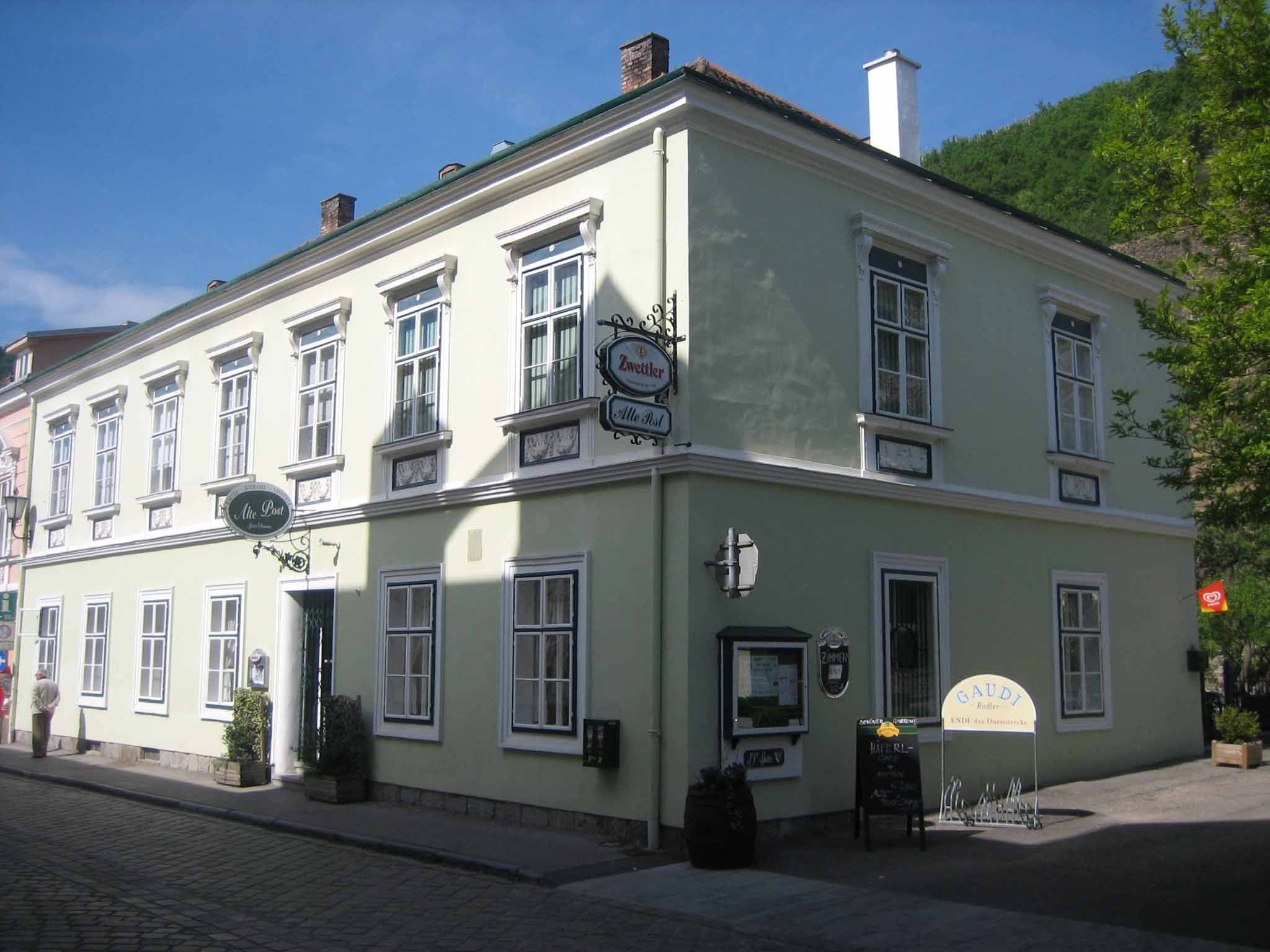 Historická budova so zelenou fasádou a niekoľkými oknami, označená ako hostinec.