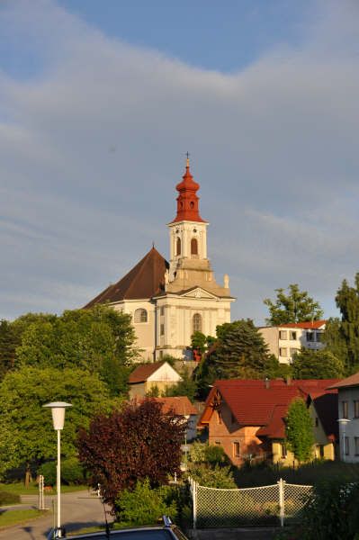 Pútnický kostol na kopci s červenými strechami a stromami v popredí.