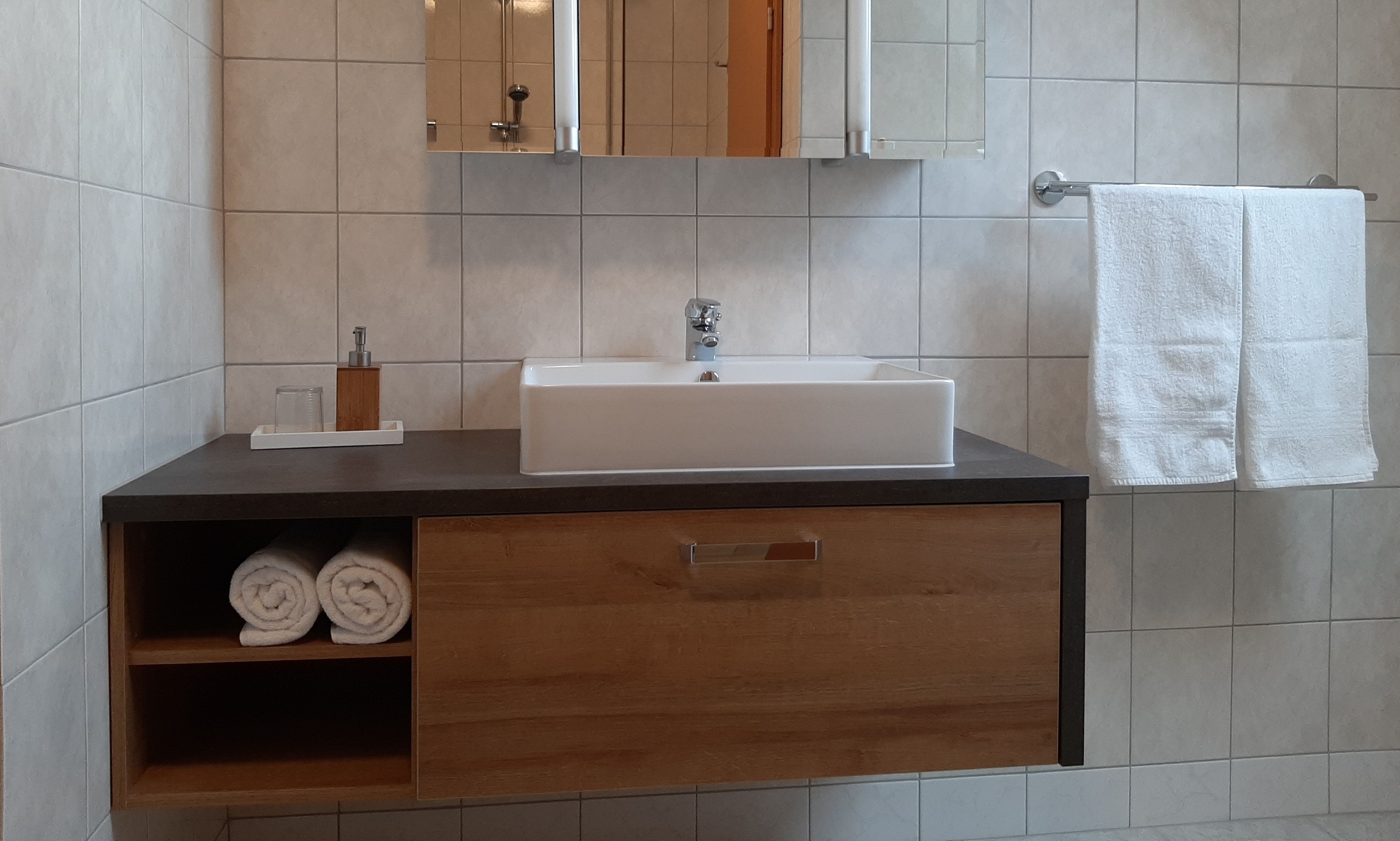 Moderná kúpeľňa s umývadlom, uterákmi a zrkadlom.