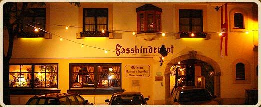 Nočný záber na budovu s označením "Fassbinderhof" osvetlenú rozprávkovými svetlami.