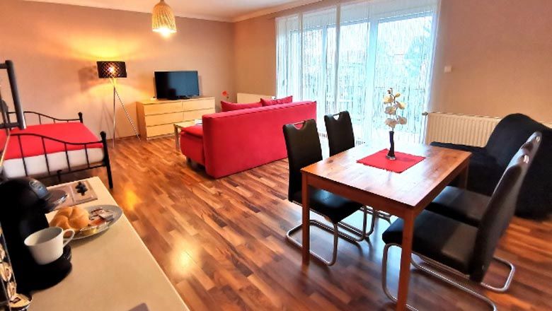 Moderná obývacia izba s červenou pohovkou, jedálenským stolom a TV s plochou obrazovkou.