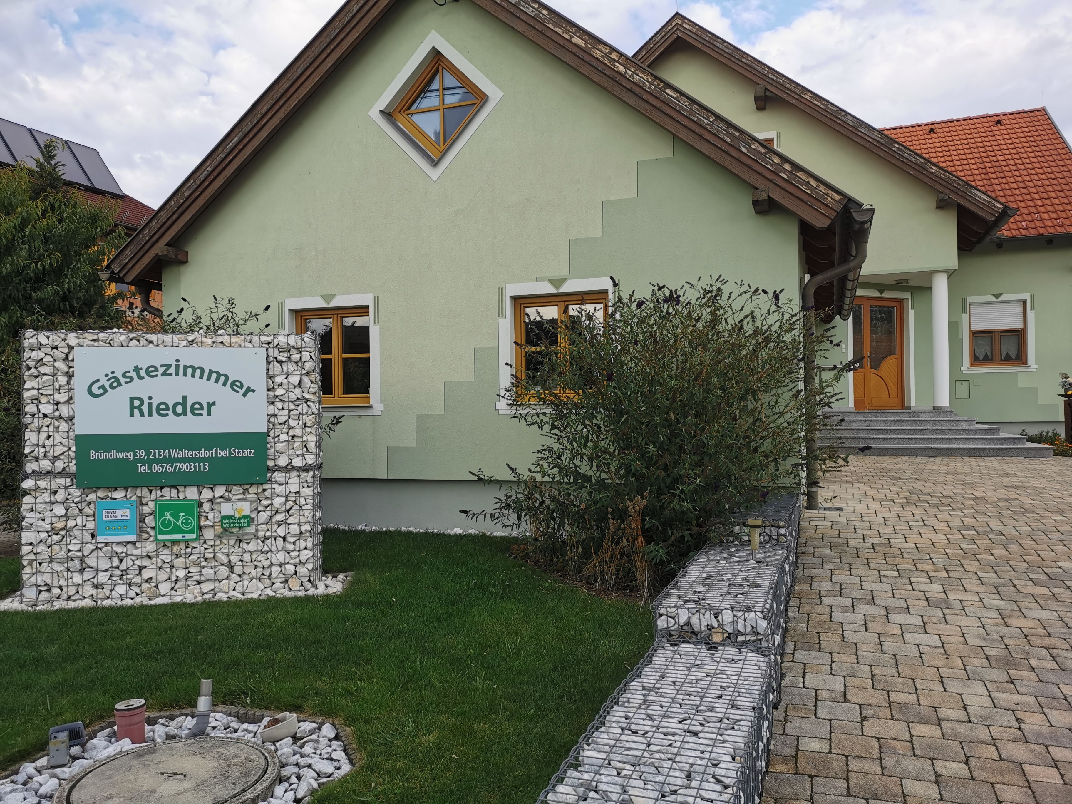 Zelený domček s nápisom "Gästezimmer Rieder" v predzáhradke.