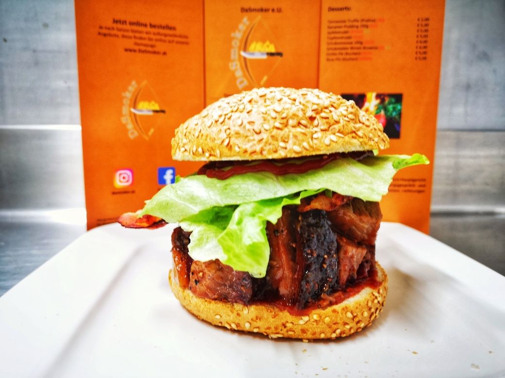 Burger so šalátom a mäsom na bielom tanieri pred oranžovým jedálnym lístkom.