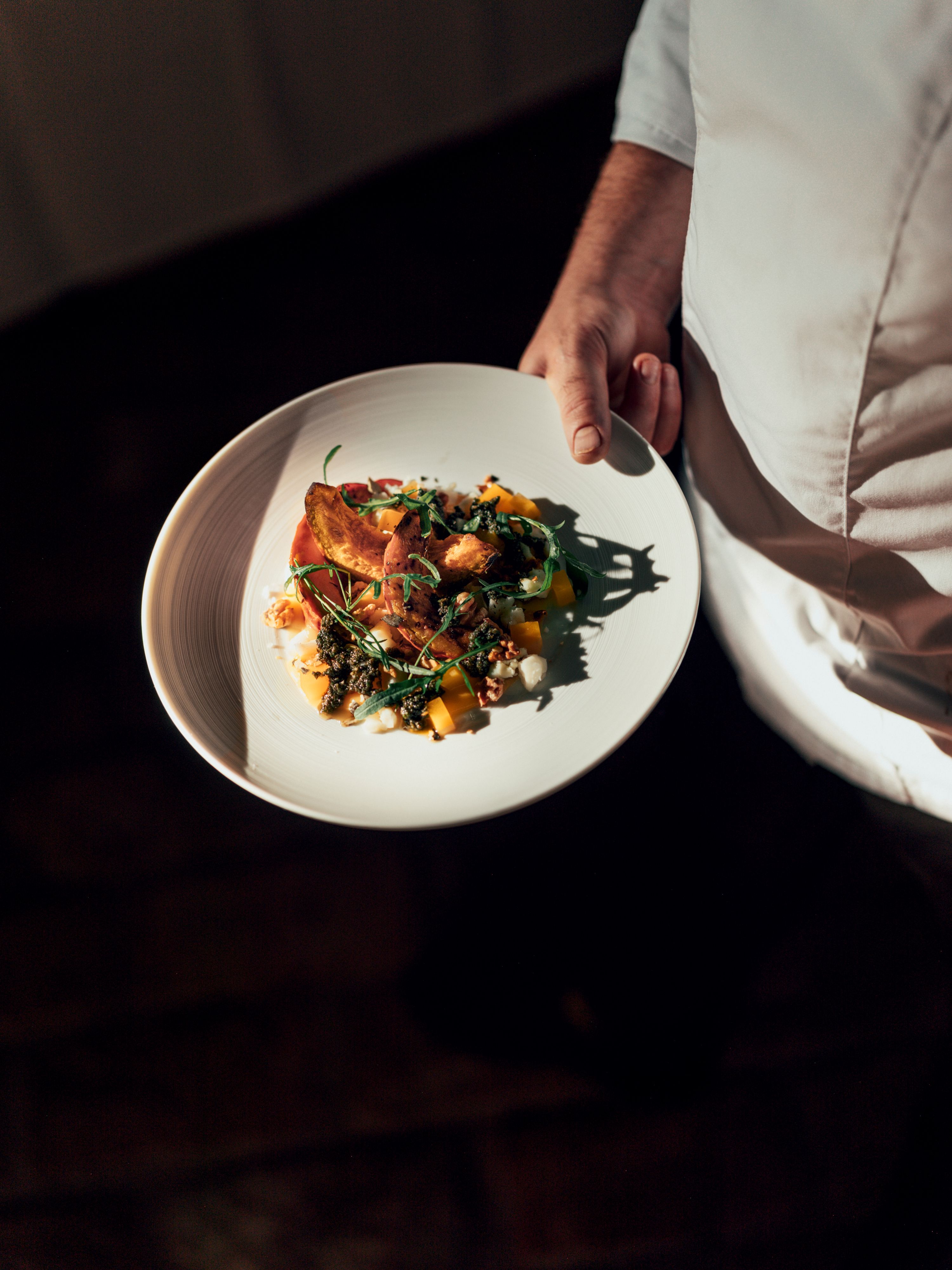 Tanier s dômyselne naaranžovaným pokrmom, ktorý drží osoba v bielom odeve.