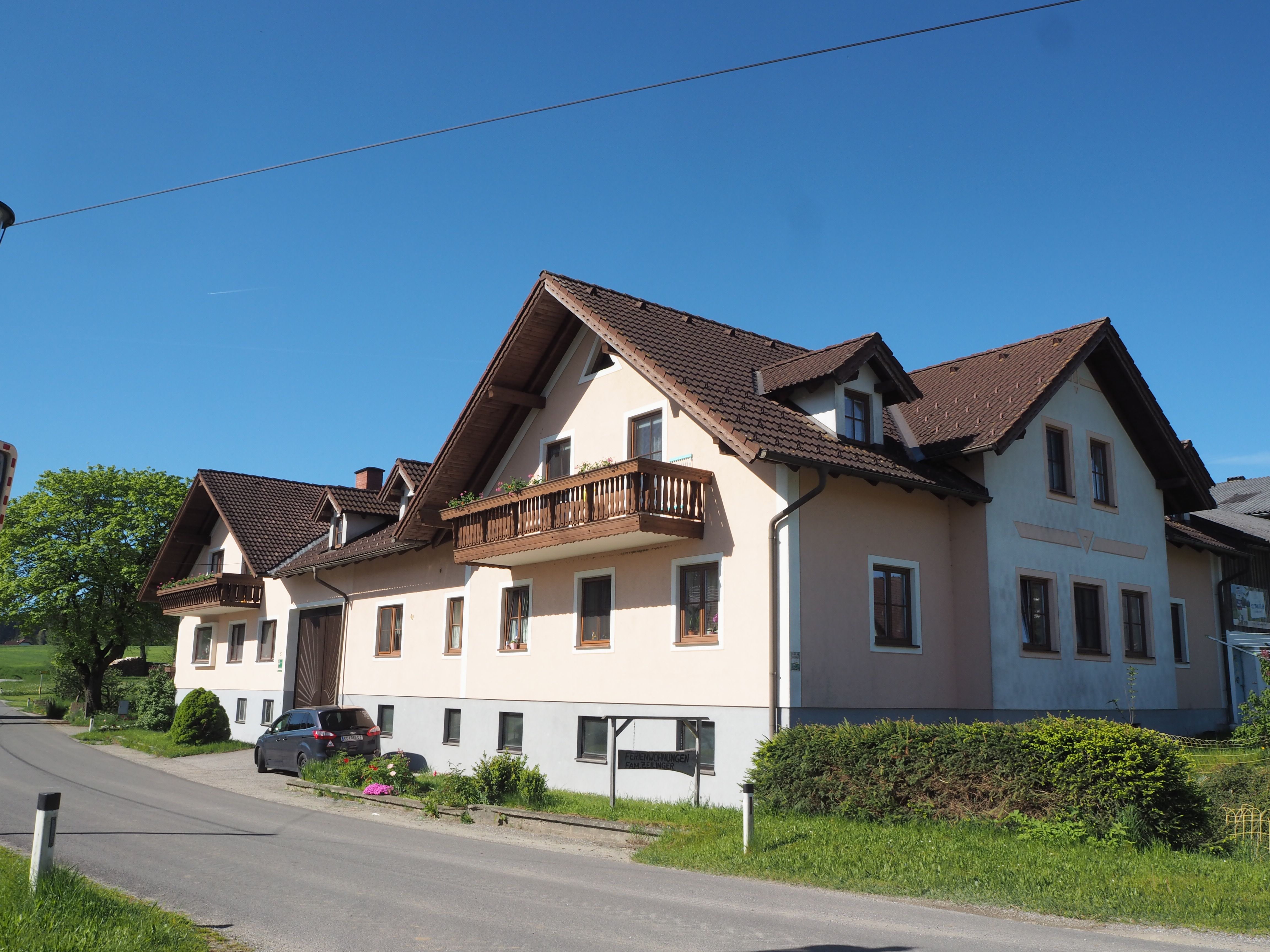 Veľký statok s hnedou strechou a balkónmi na vidieckej ceste pod jasnou oblohou.