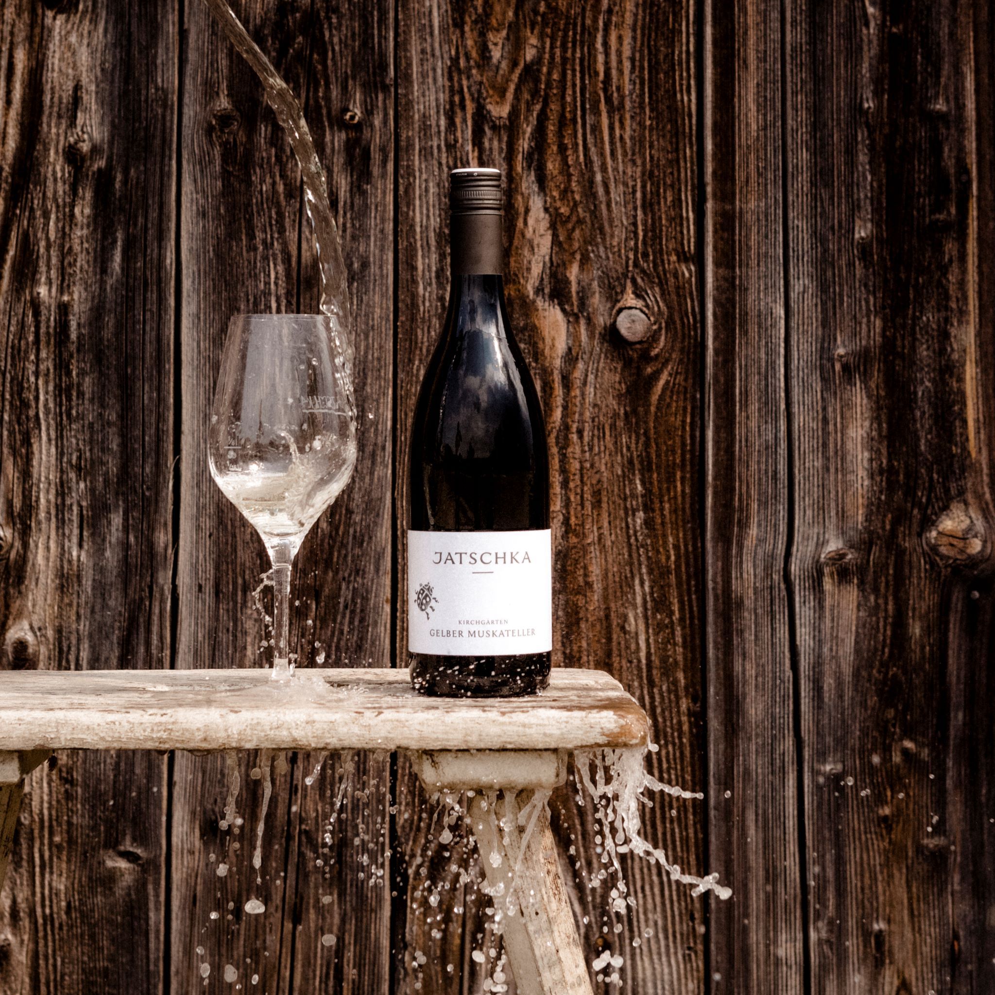 Fľaša vína a pohár s vodou pred drevenou stenou.