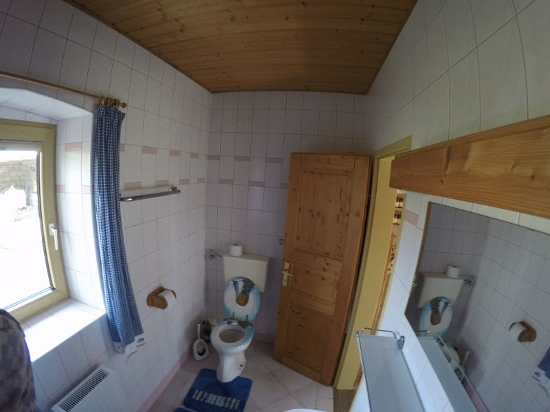 Kúpeľňa s WC, dreveným stropom a oknom s modrým závesom.