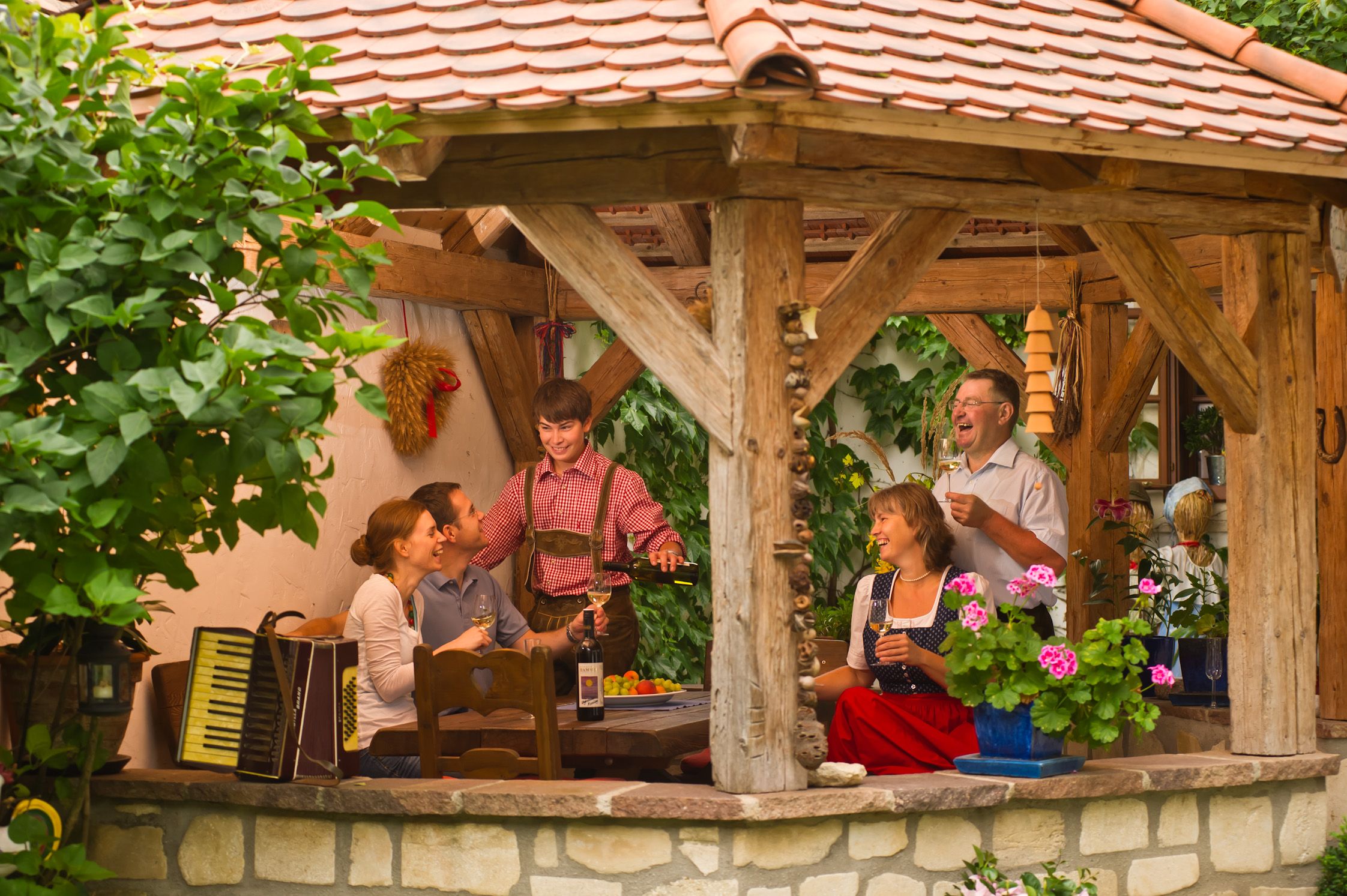 Skupina ľudí sedí v krytom rustikálnom pavilóne a vychutnáva si víno a spoločnosť.