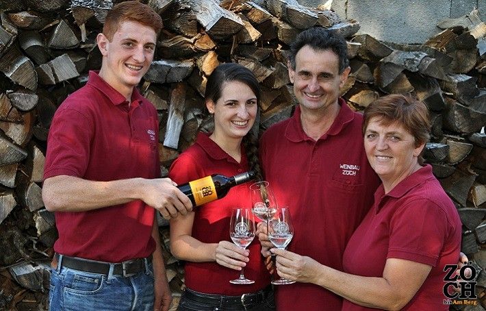 Štyria ľudia v červených košeliach si cinknú pohárom vína pred hromadou polien.