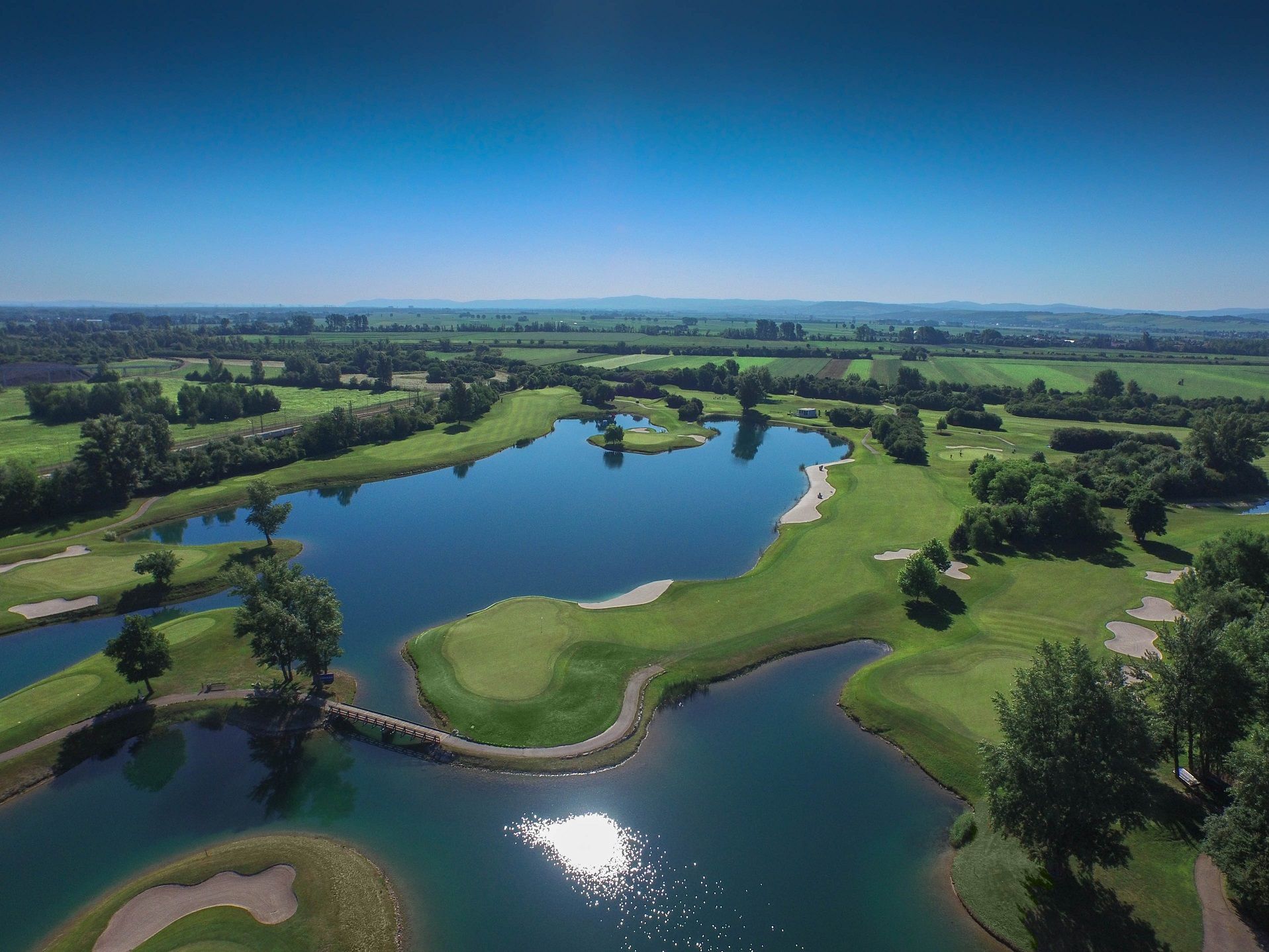 Letecký pohľad na golfové ihrisko s vodnými prekážkami a zelenými dráhami.