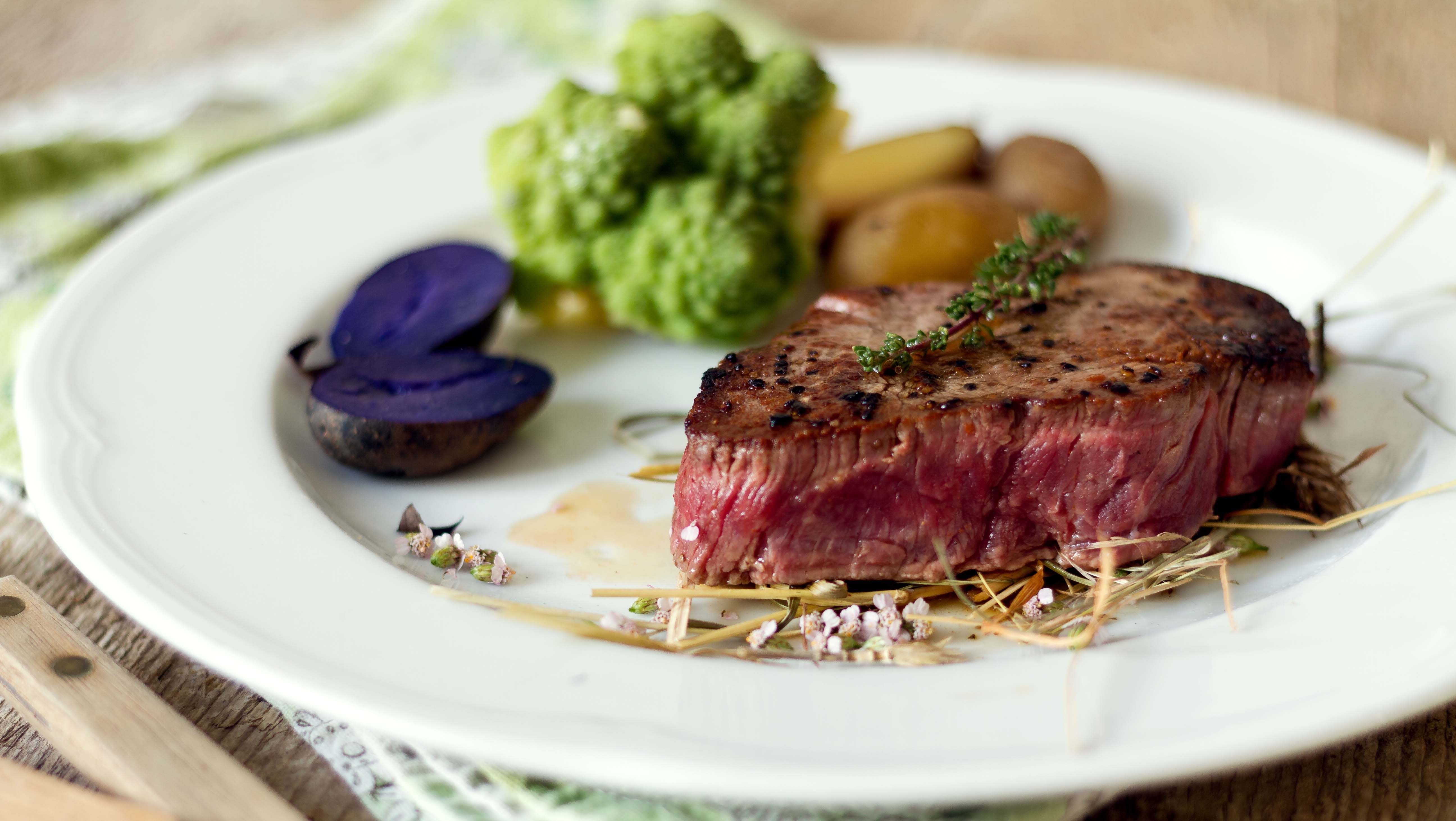 Kúsok steaku na bielom okrúhlom tanieri so zeleninou, zemiakmi a bylinkami.