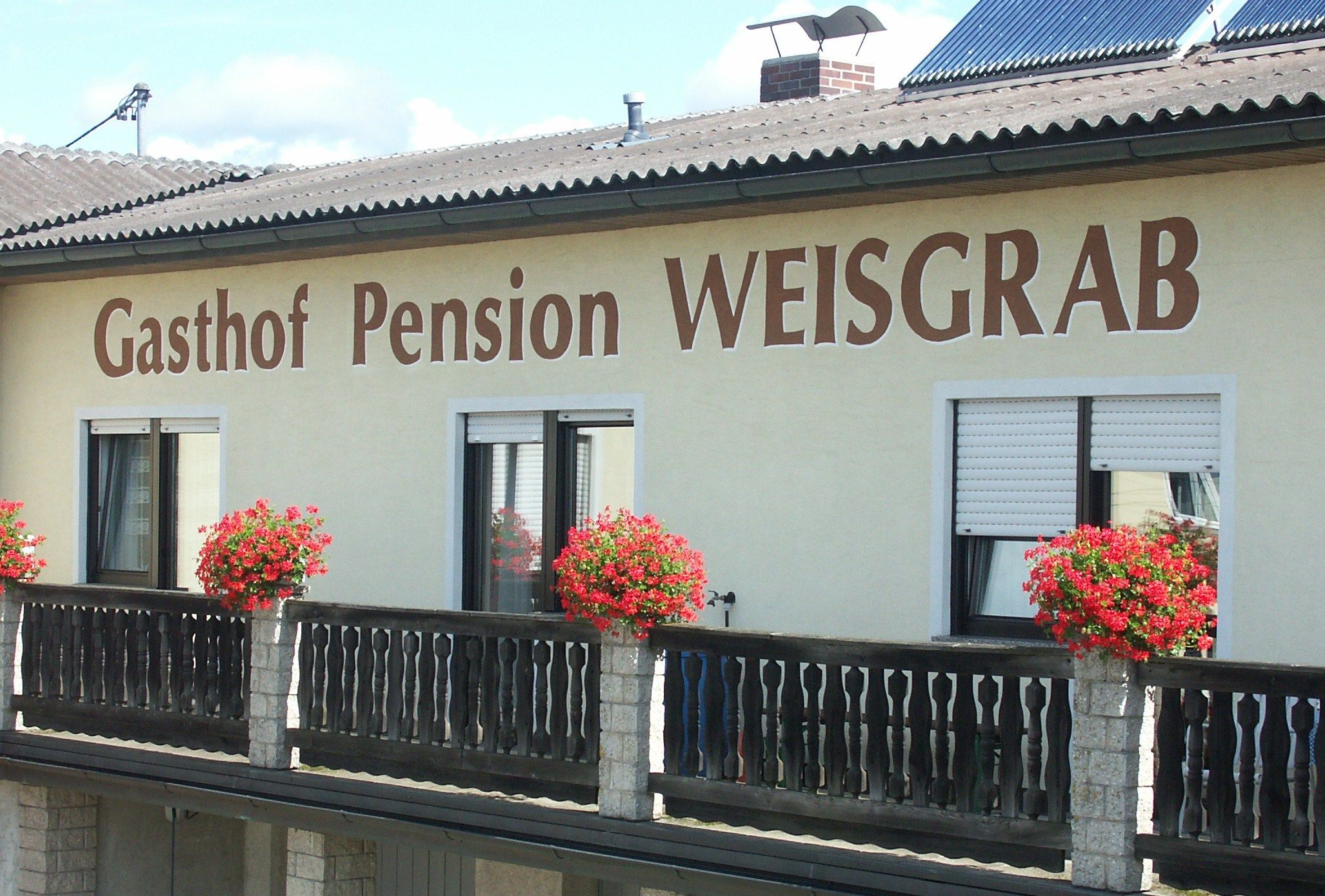 Fasáda penziónu Weisgrab s kvetinovými truhlíky na balkóne.