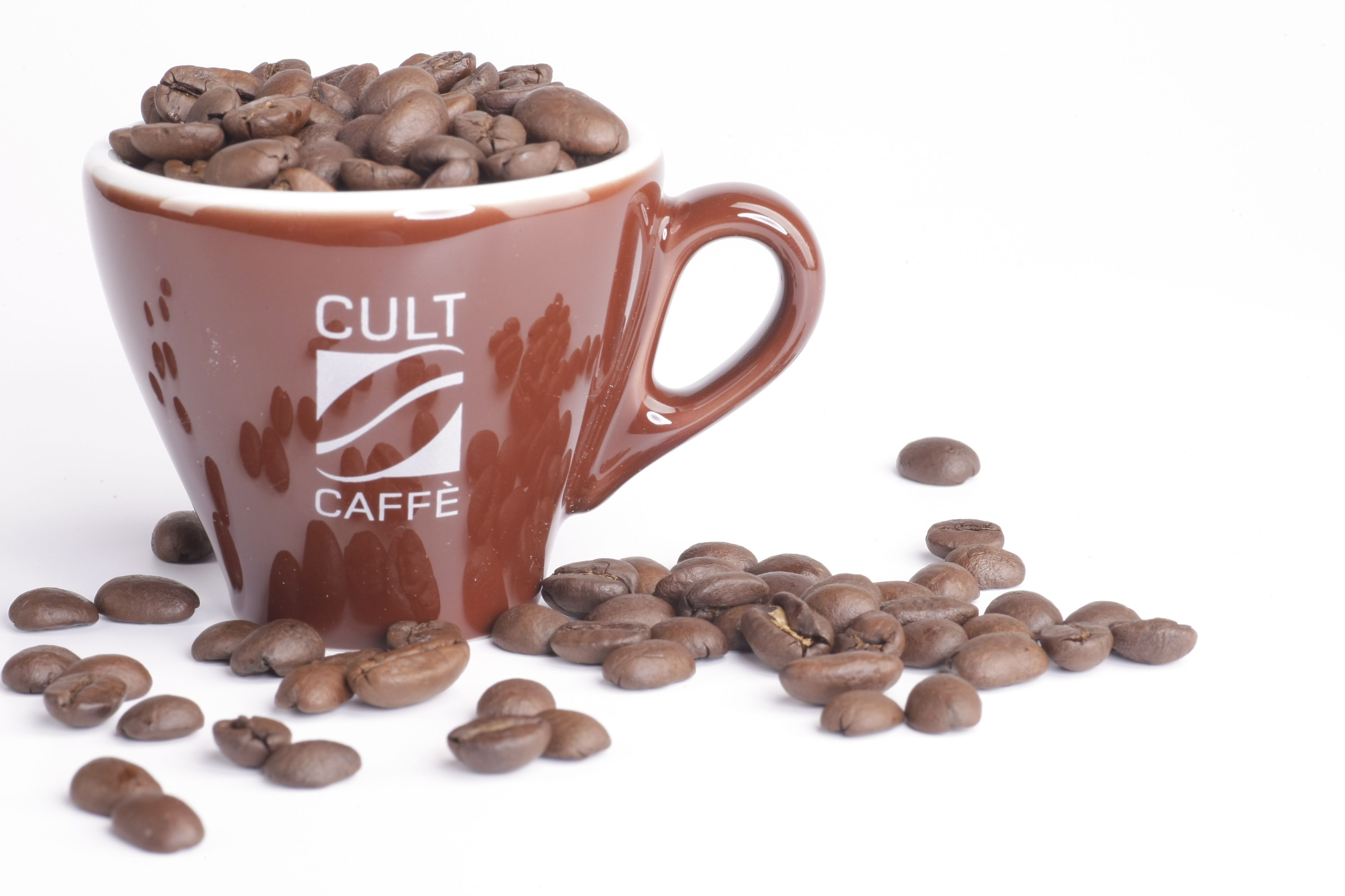 Hnedý hrnček s nápisom "Cult Caffè", naplnený zrnkovou kávou, na bielom pozadí.