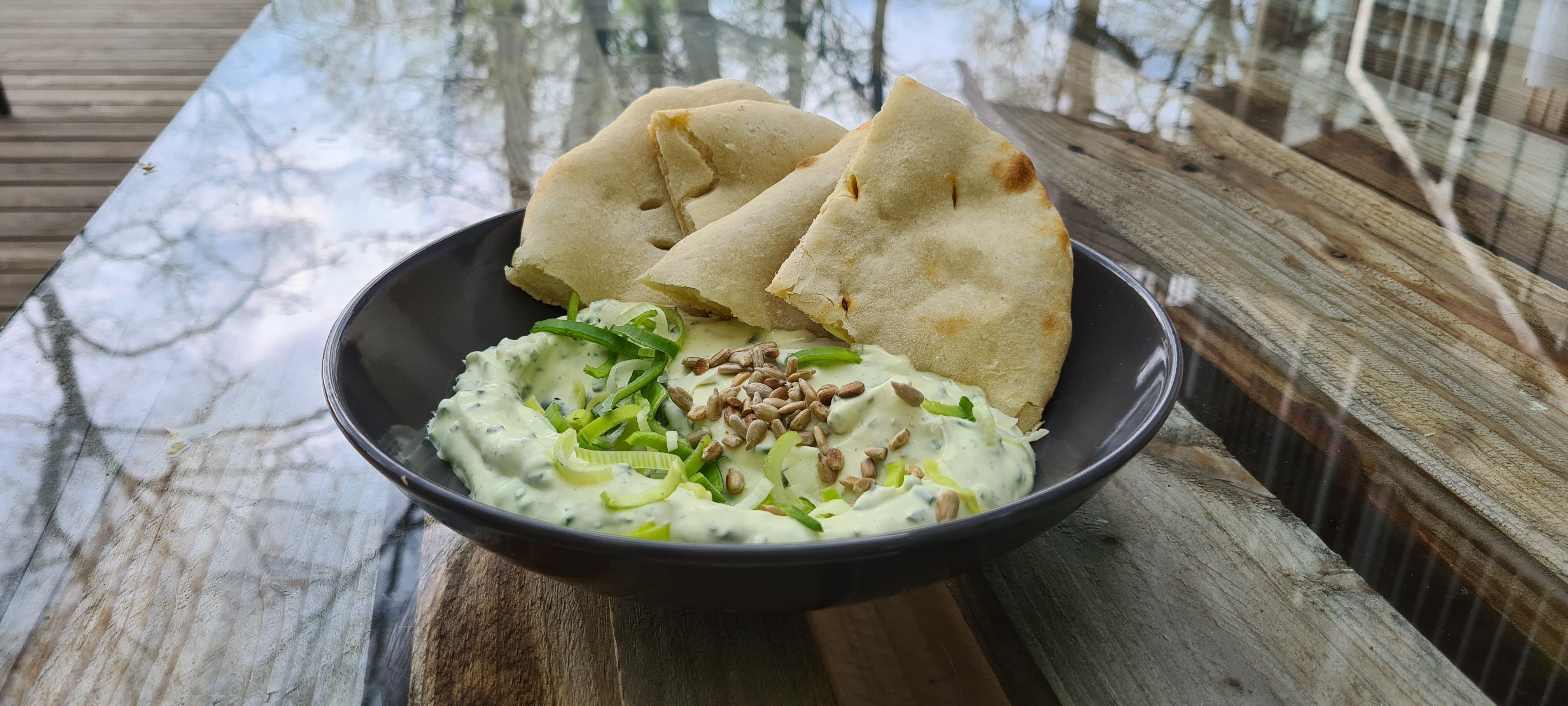 Čierna miska s dipom a kúskami chleba na drevenom stole.