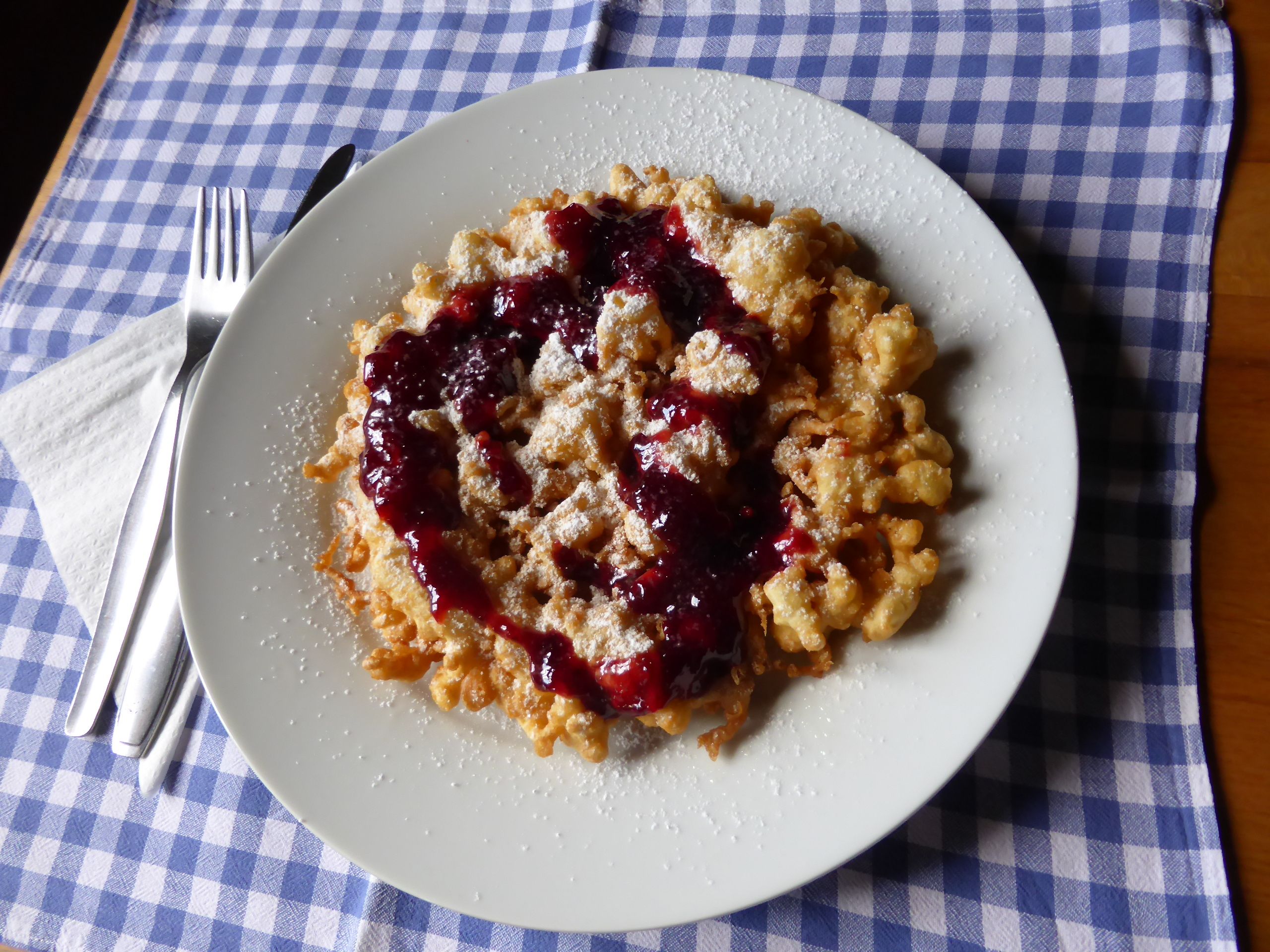 Tanier Kaiserschmarrn a červené ovocné želé na modro-bielej károvanej látke.
