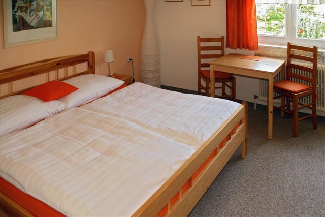 Útulná izba pre hostí s manželskou posteľou, dreveným nábytkom a malým stolíkom pri okne.