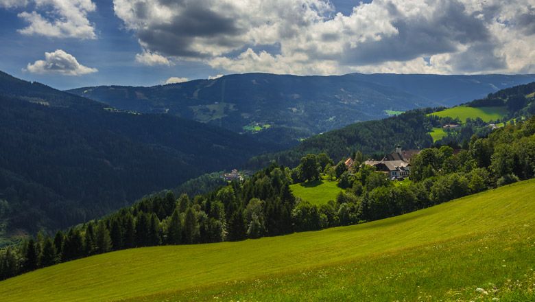 Zelené kopce a lesy v hornatej krajine pod zamračenou oblohou.