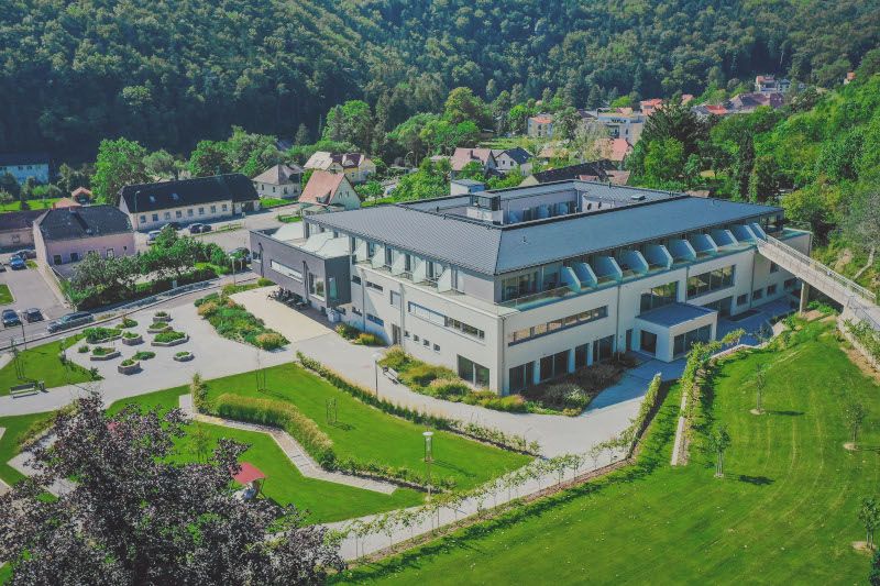Letecký pohľad na modernú budovu so záhradou a okolitou krajinou.