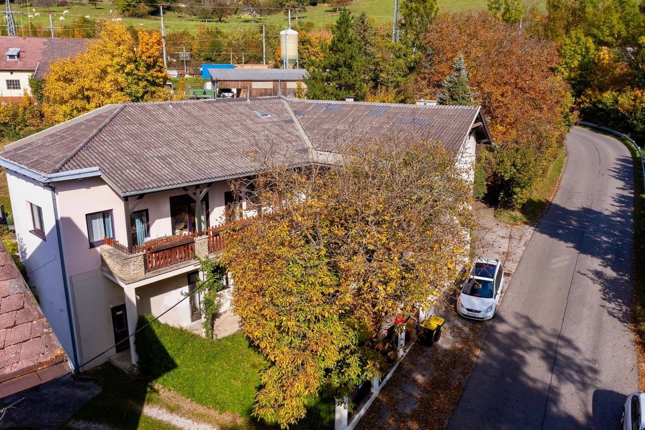Letecký pohľad na dvojpodlažnú budovu s balkónom, obklopenú jesennými stromami a ulicou.