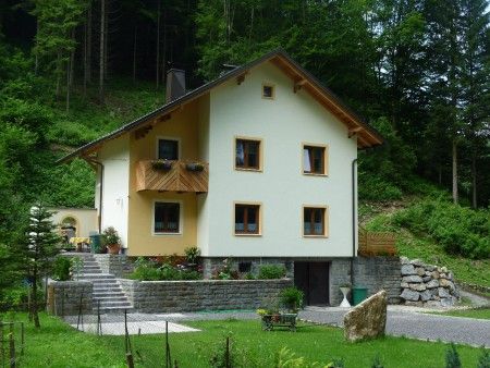 Žltý penzión s dreveným balkónom, obklopený zelenou prírodou a stromami.