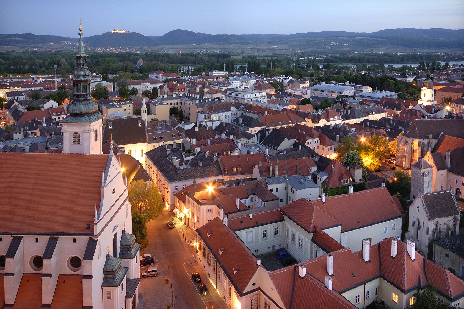 Večerný pohľad na Krems s osvetlenými budovami a kopcami v pozadí.