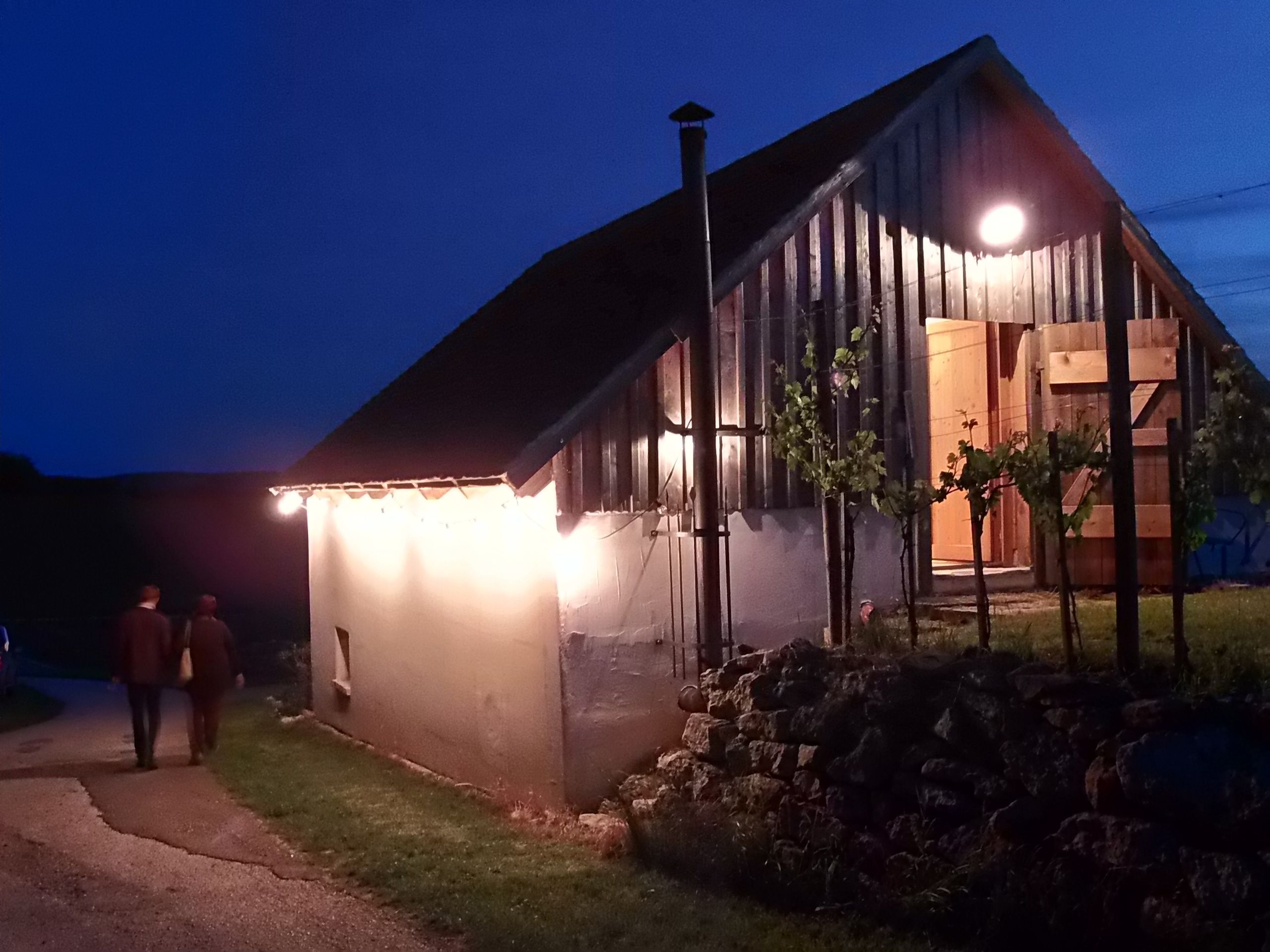 Osvetlená budova vínnej pivnice v noci s dvoma ľuďmi na ceste.