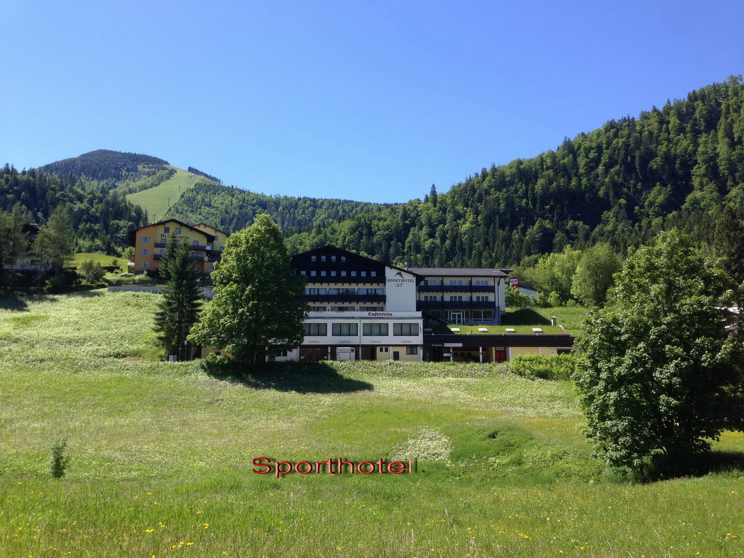 Športový hotel v zelenej horskej krajine s modrou oblohou.