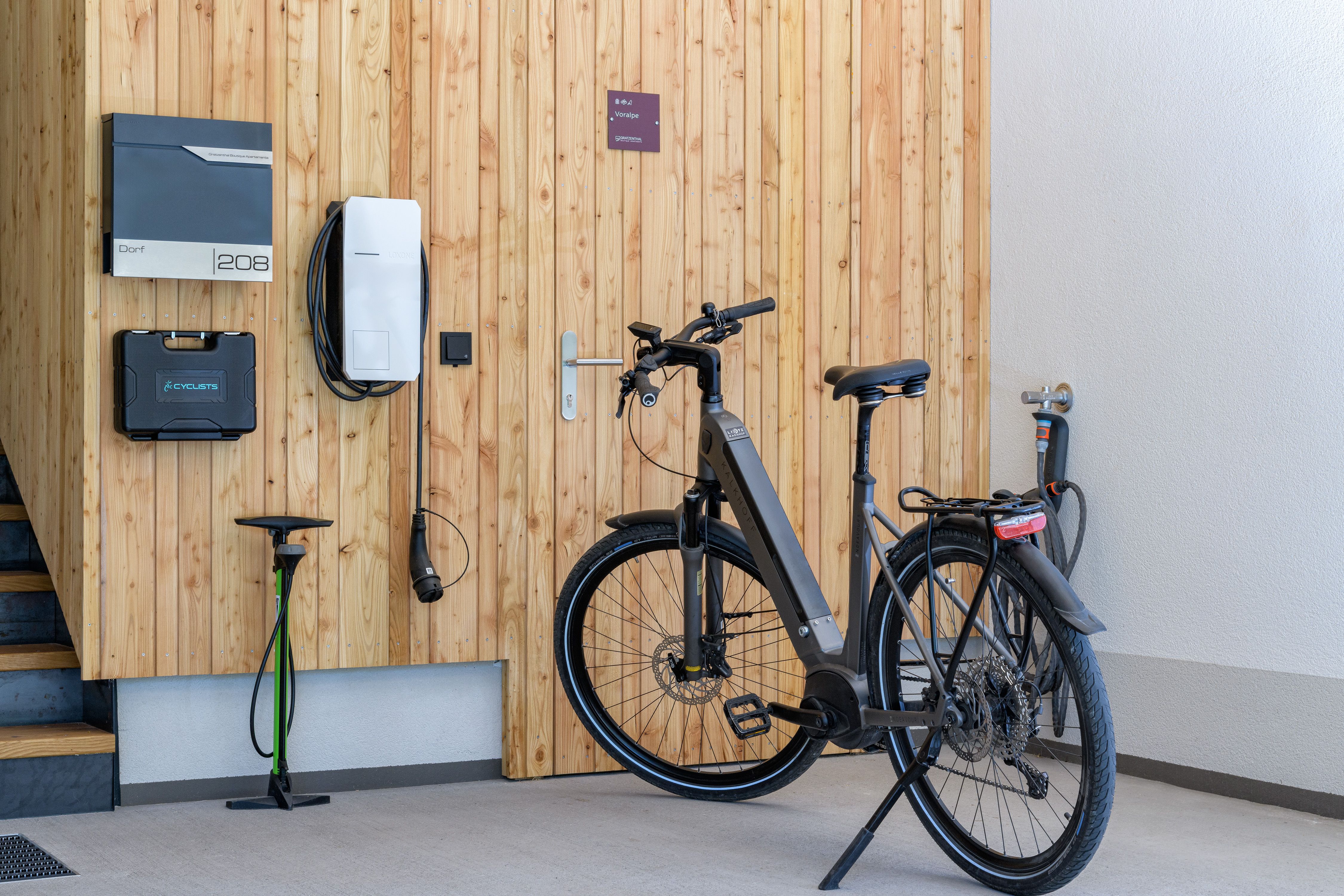 V garáži stojí moderný elektrobicykel vedľa nabíjacej stanice pri drevenej stene.