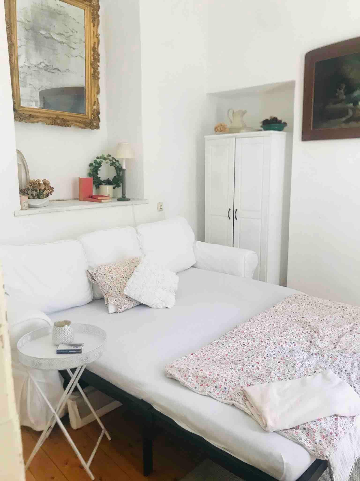 Útulný priestor na spanie s bielou pohovkou, príručným stolíkom a dekoratívnymi prvkami.