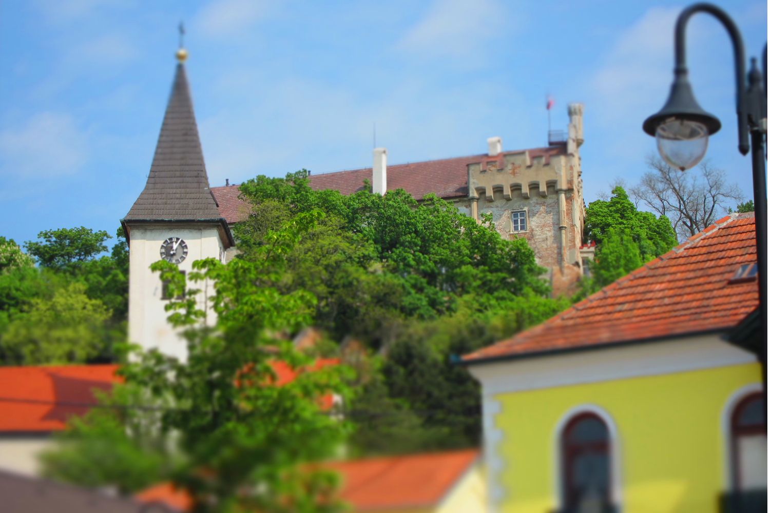 Kostolná veža a hrad za stromami, modrá obloha.