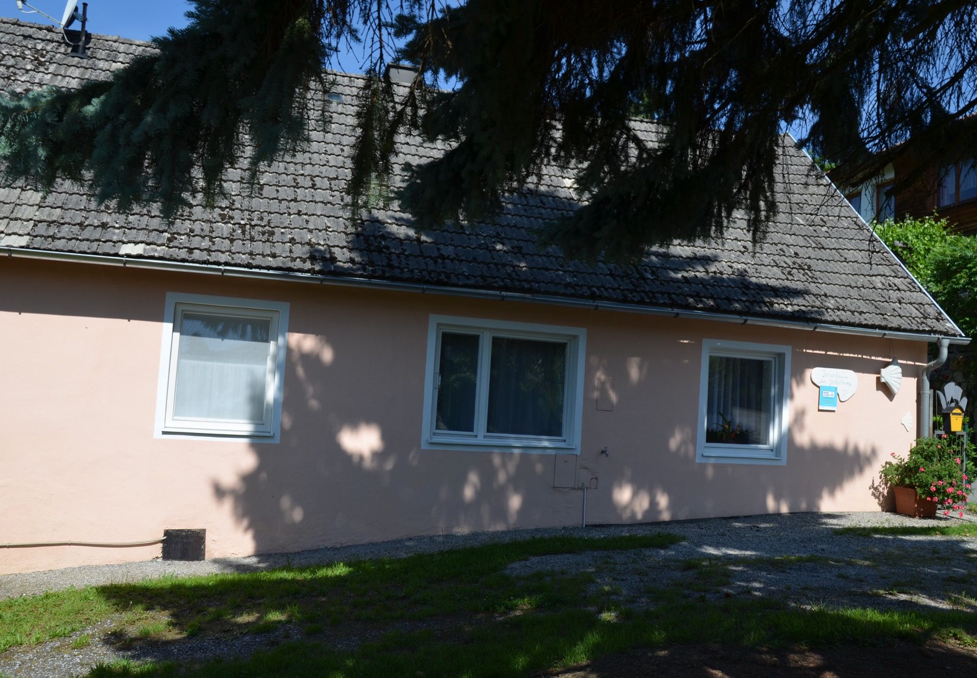 Malý ružový prázdninový dom s tienistými stromami v popredí.