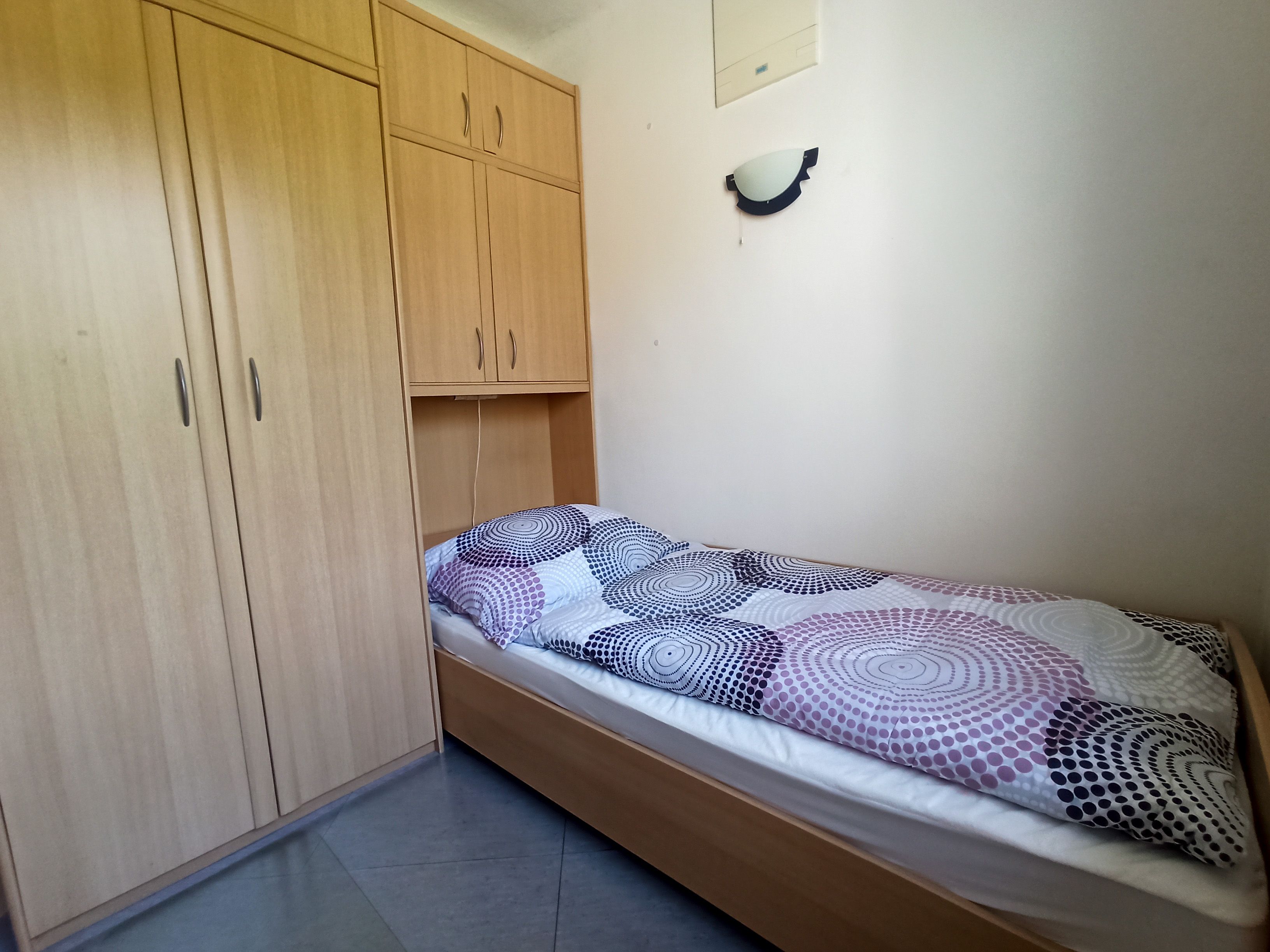 Jednoduchá spálňa s jednou posteľou a veľkou drevenou skriňou.