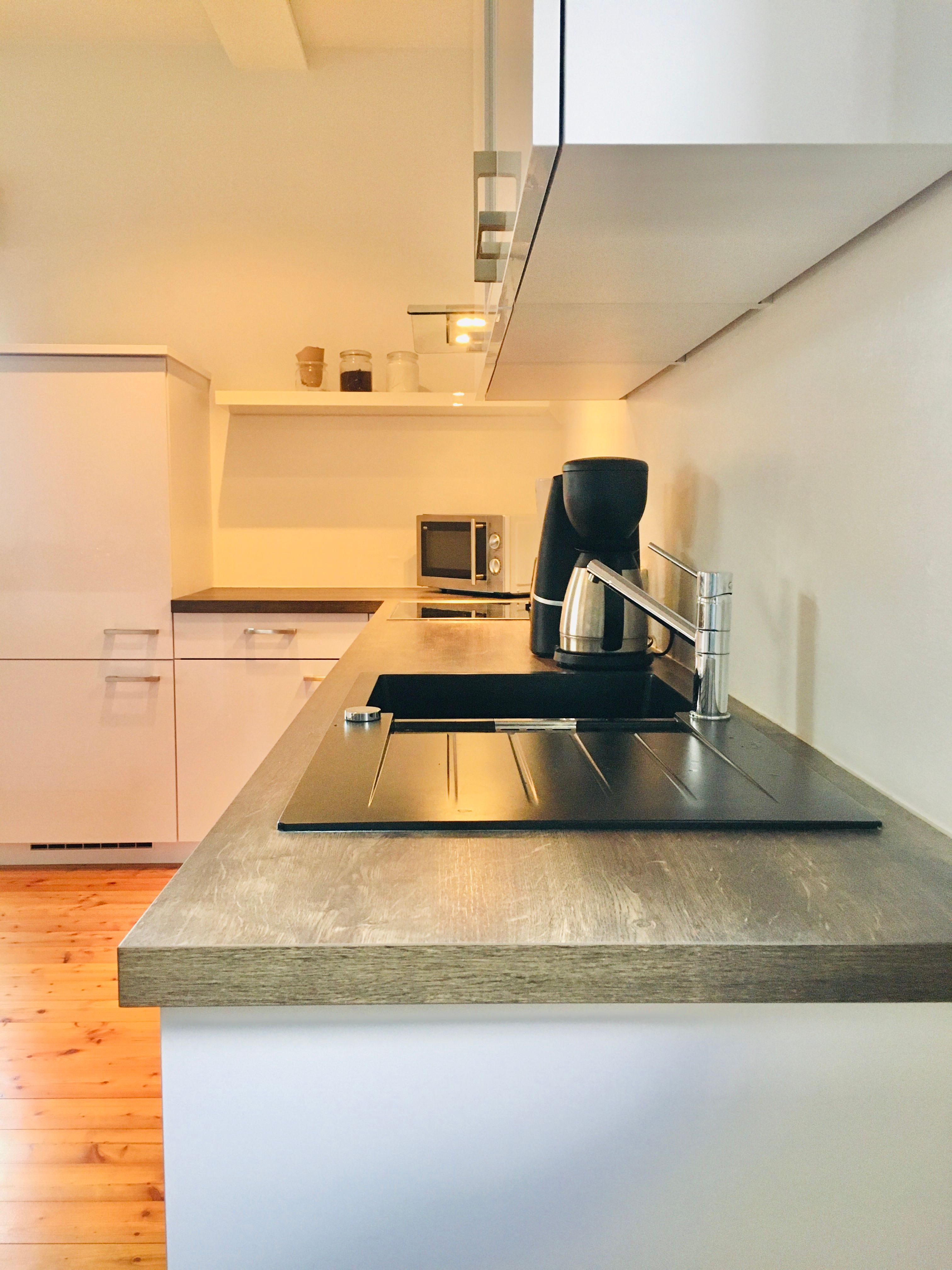 Moderná kuchyňa s drevenou pracovnou doskou, drezom, kávovarom a mikrovlnnou rúrou.