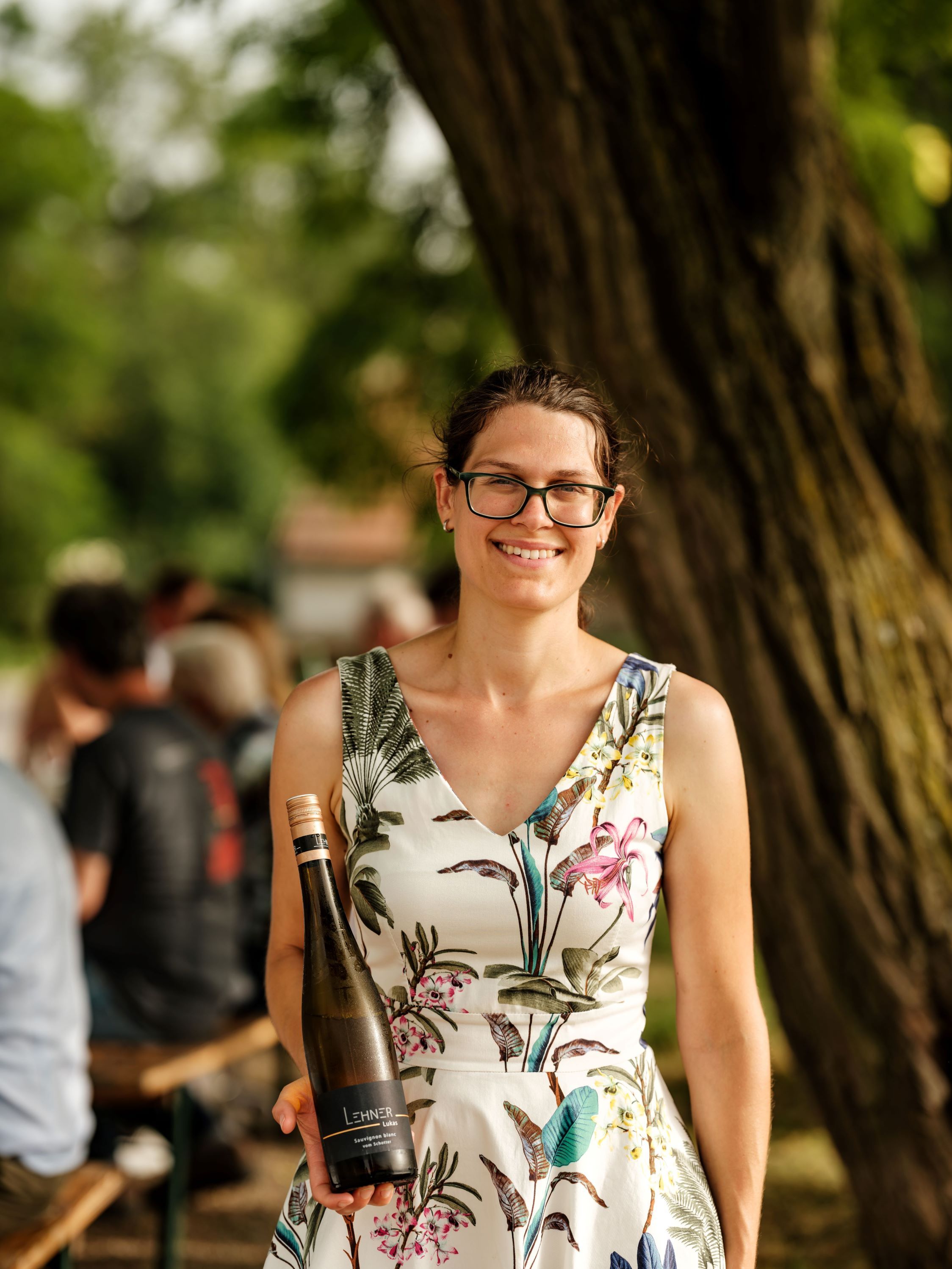 Žena s okuliarmi drží fľašu vína v exteriéri.
