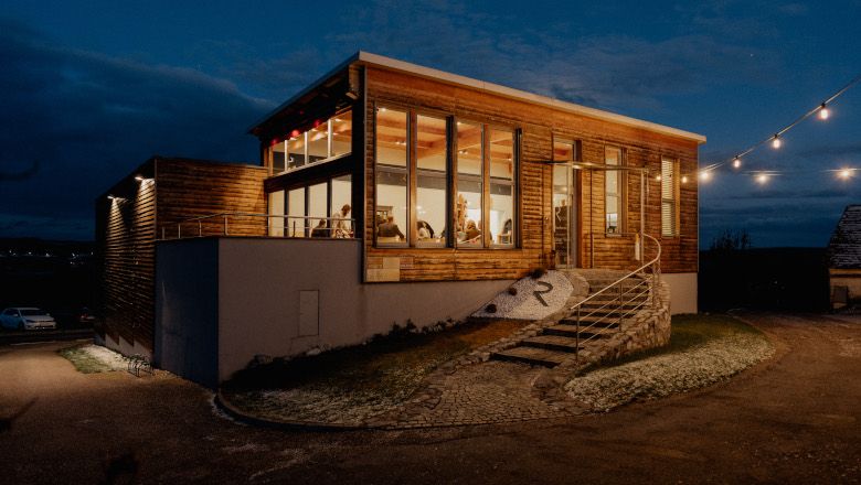 Exteriérový pohľad na modernú vinotéku v noci s osvetlenými oknami a rozprávkovými svetlami.