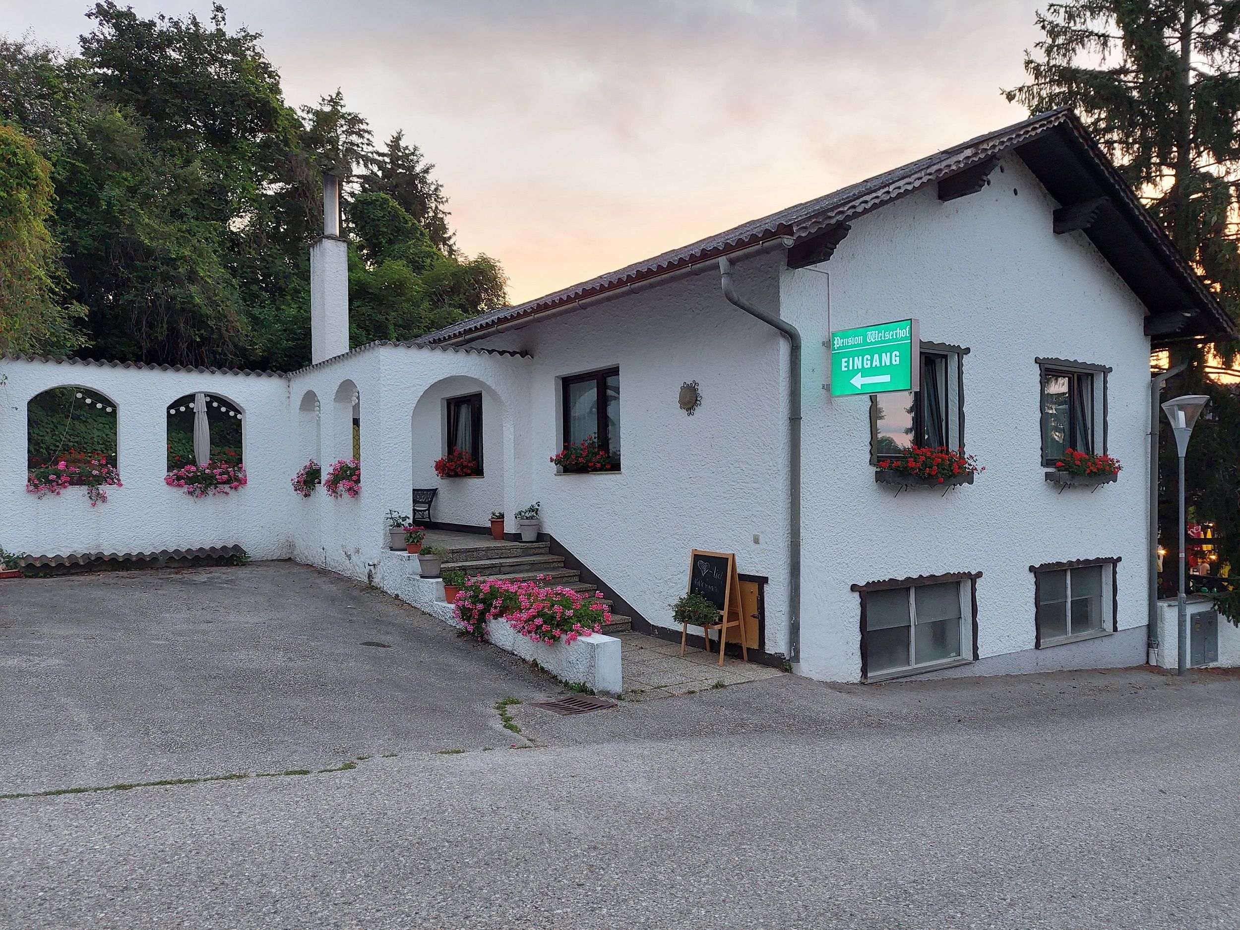 Pohľad zvonku na bielu budovu s kvetmi a nápisom "Pension Welserhof Eingang".