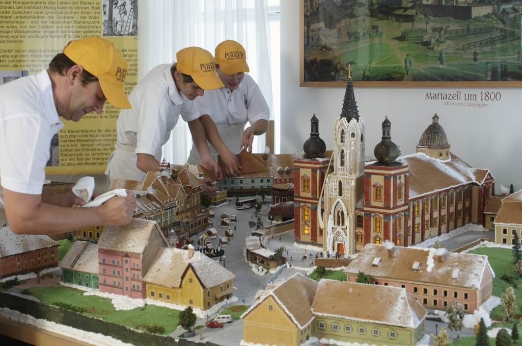 Tri osoby zdobia perníkový model Mariazellu okolo roku 1800.