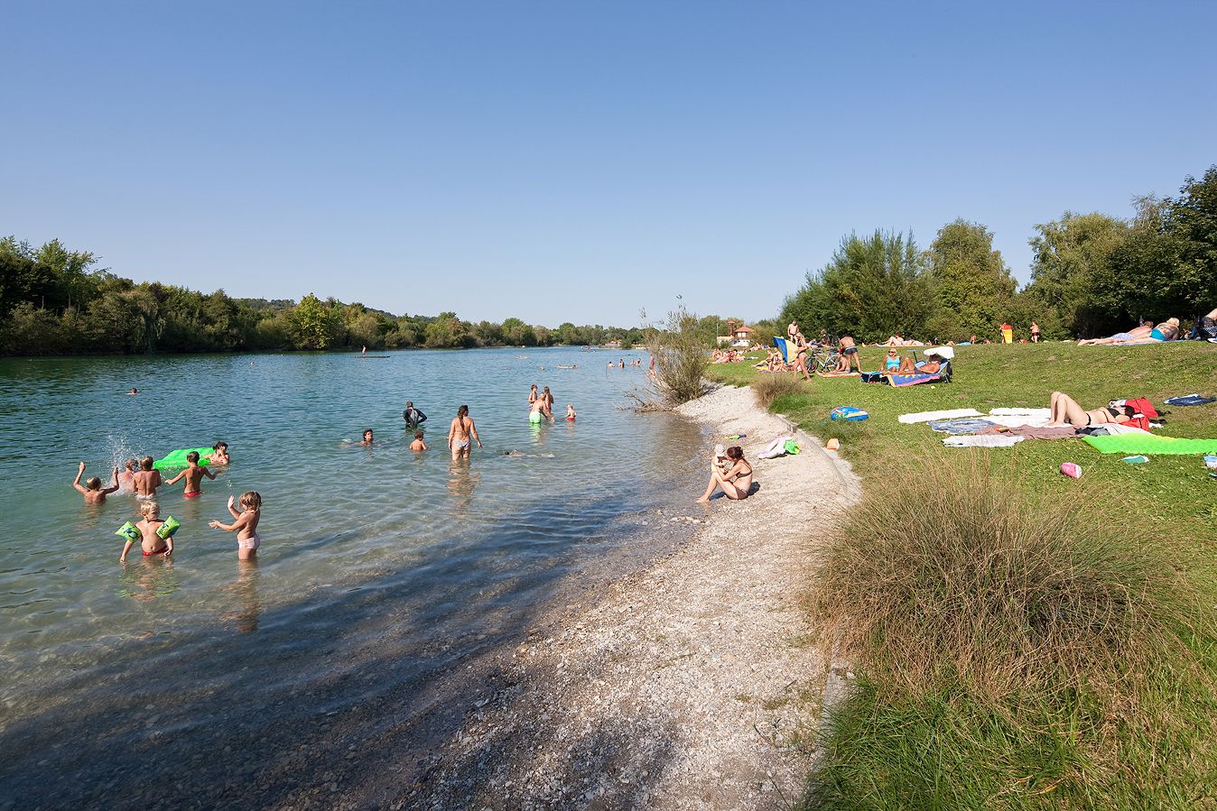 Ľudia sa počas slnečného dňa kúpu a relaxujú pri jazere Ratzersdorf.