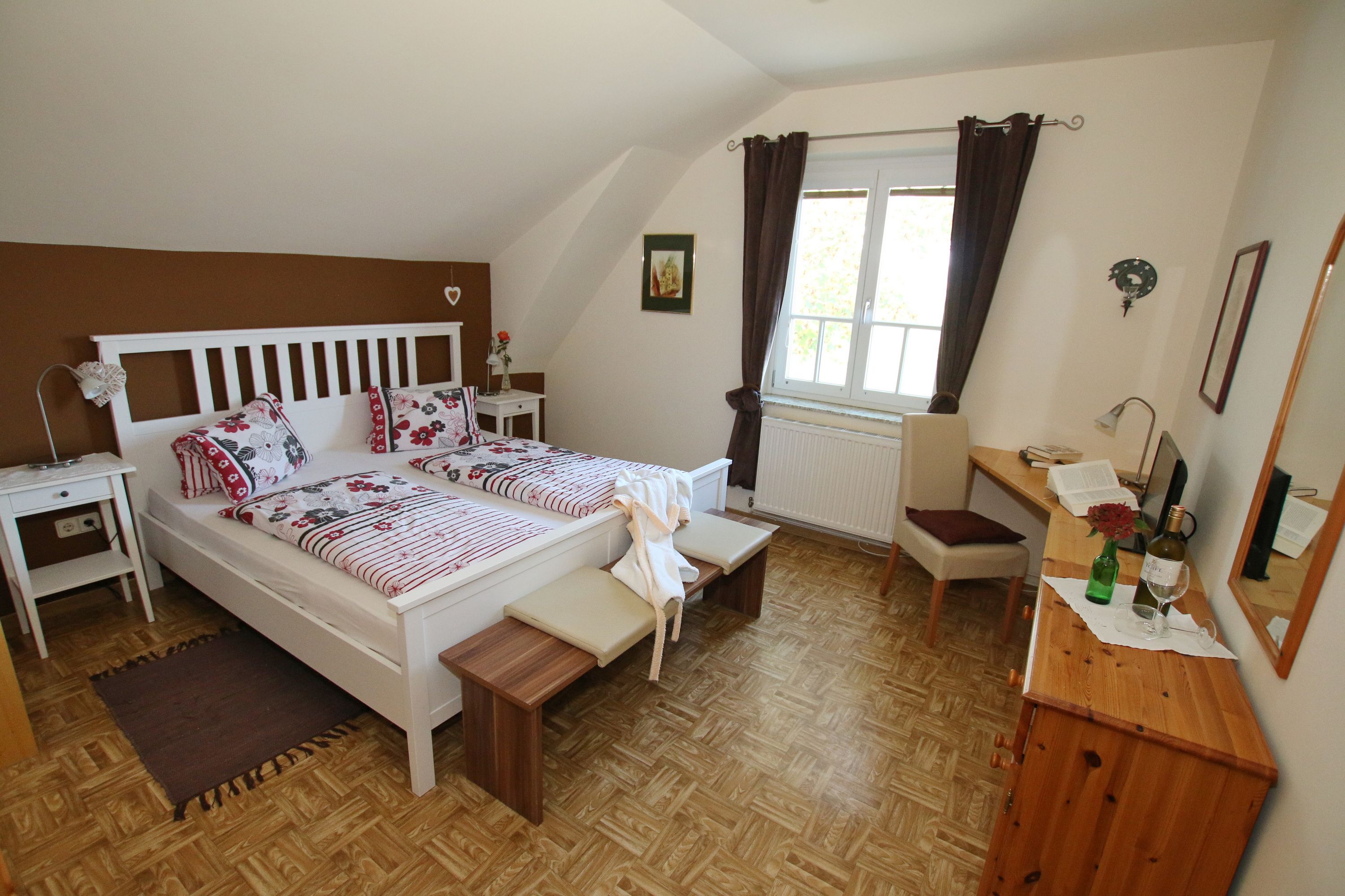 Útulná izba pre hostí s manželskou posteľou, pohovkou, stolom a stoličkou. Hnedá akcentová stena a tmavé závesy.