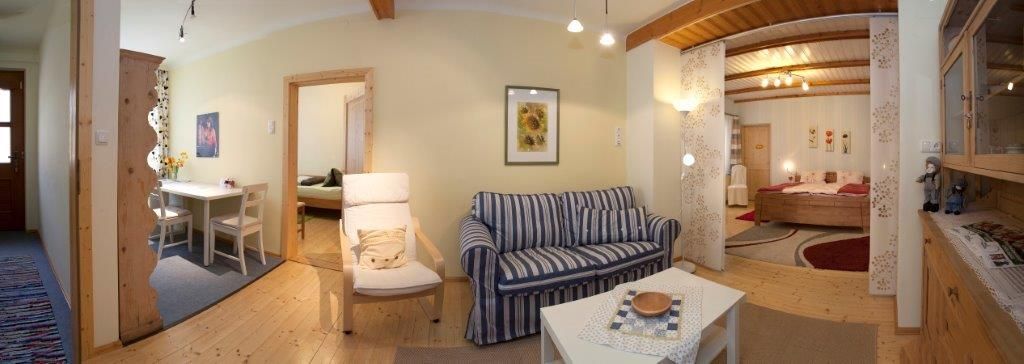 Panoráma útulnej obývačky s pohovkou, jedálenským stolom a spálňou v pozadí.