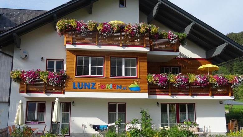 Rekreačný dom s farebnými kvetmi na balkónoch a nápisom "LUNZ Ferien".