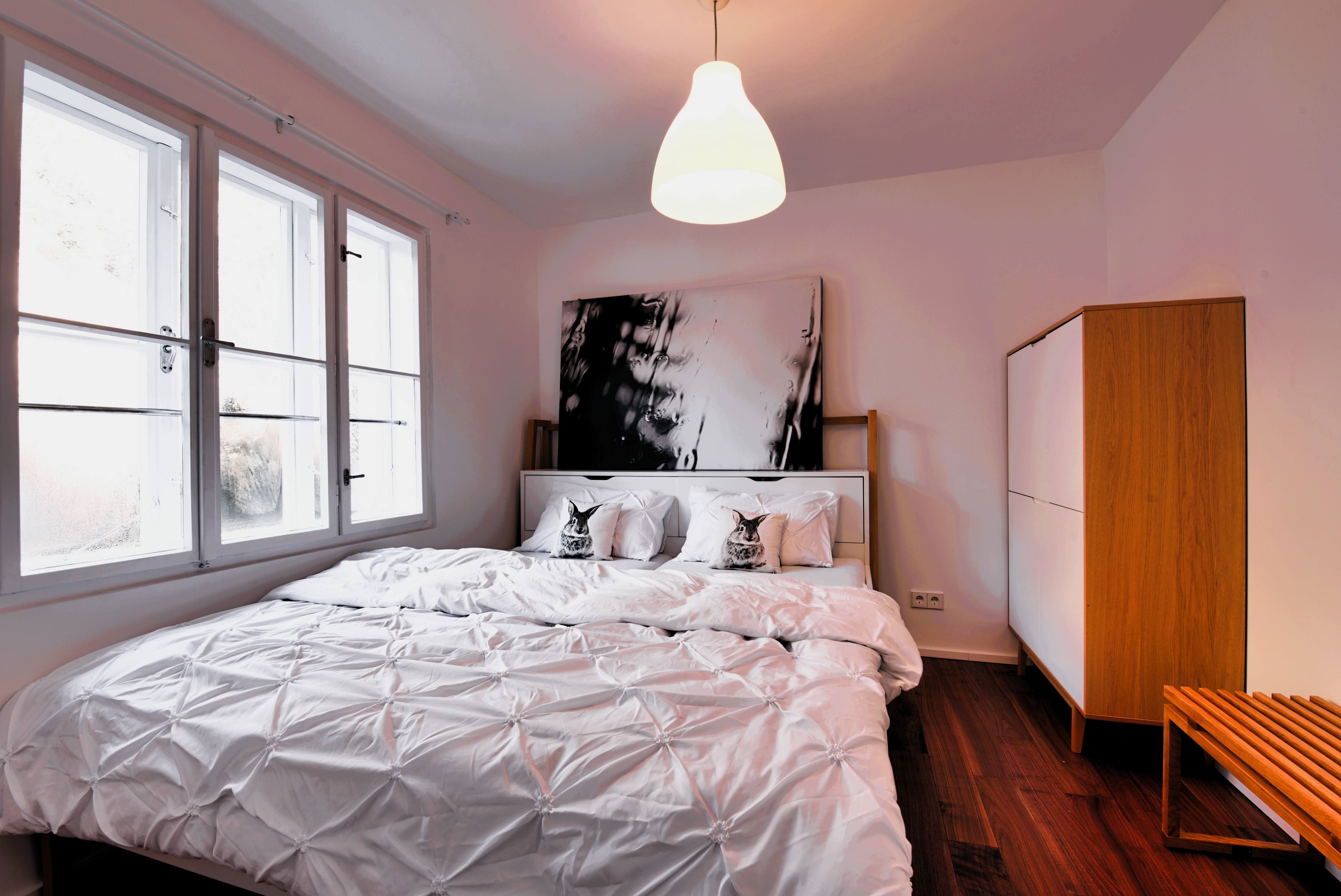 Moderná spálňa s veľkou posteľou, bielou posteľnou bielizňou a drevenou skriňou.