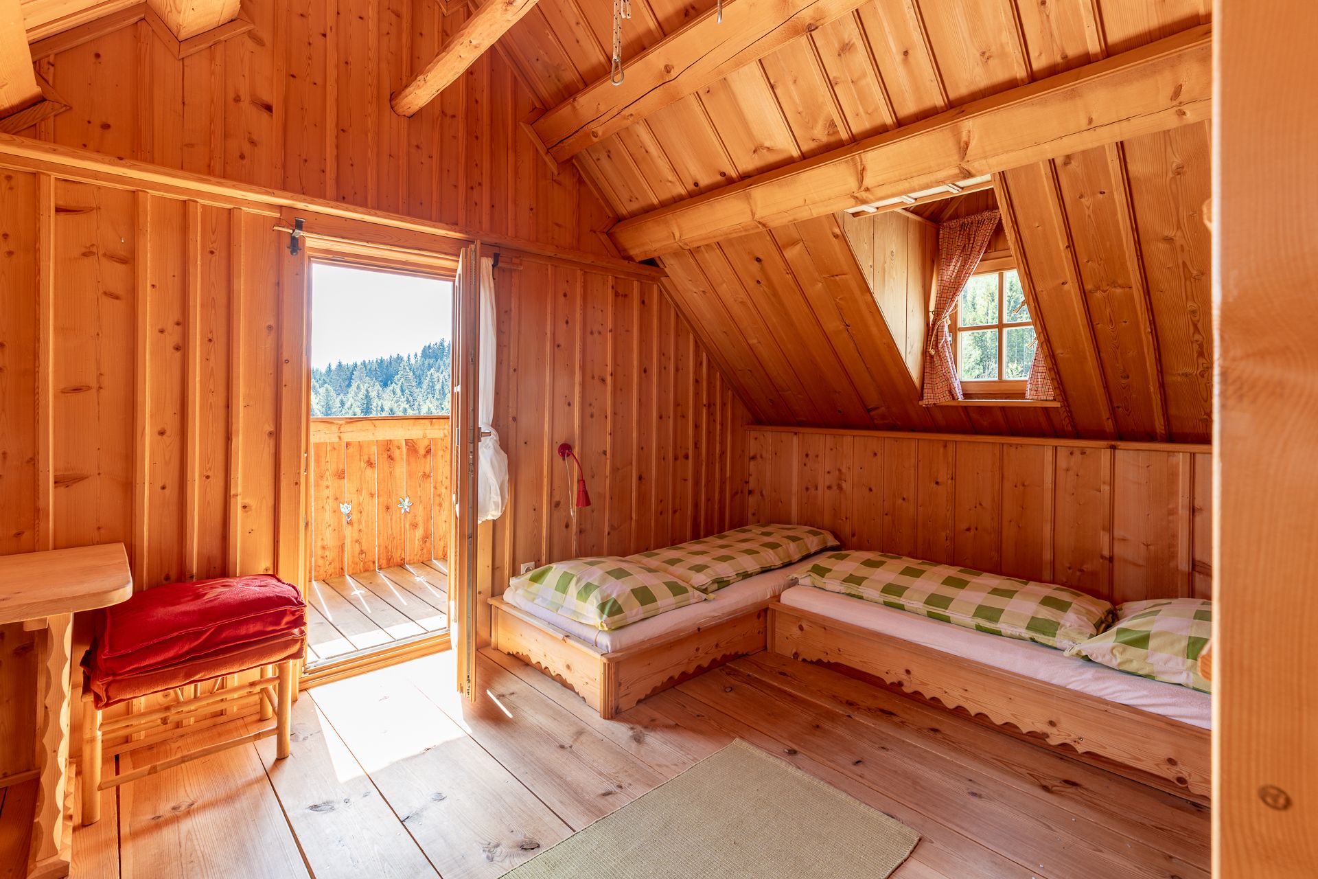 Spálňa s dreveným obložením, dvoma posteľami, oknom a otvorenými dverami na balkón.