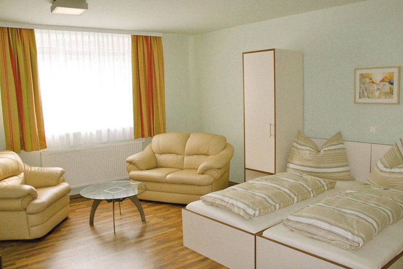 Svetlá izba s dvoma posteľami, pohovkami, stolom a šatníkovou skriňou.