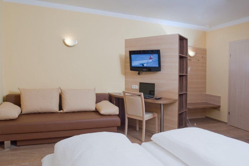 Hotelová izba s pohovkou, stolom, televízorom a posteľou.