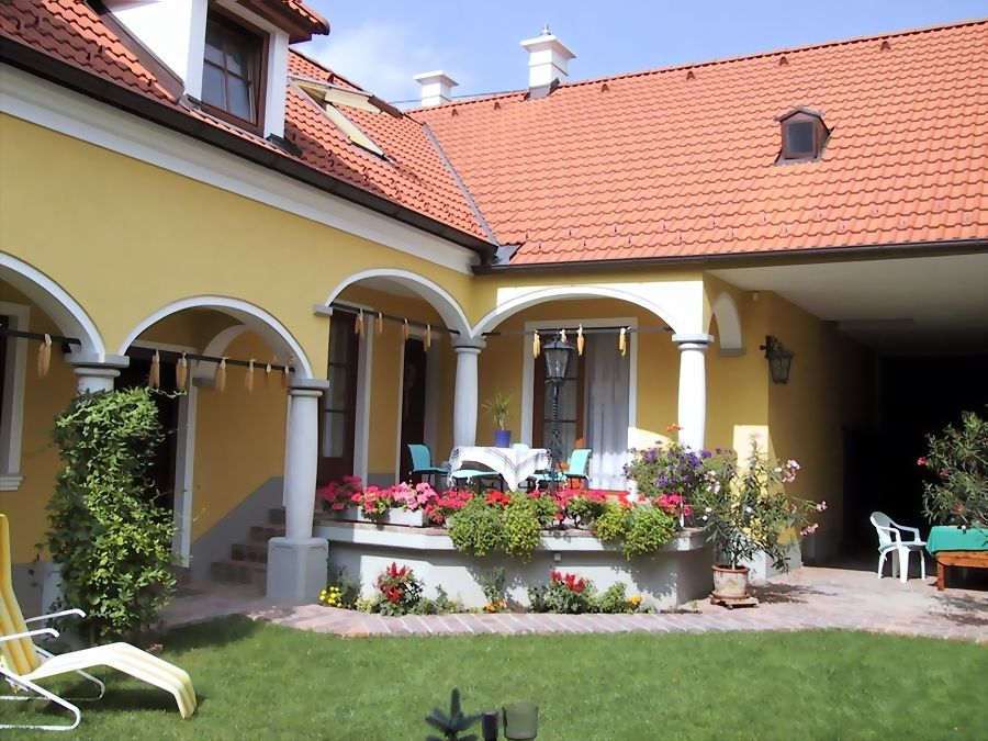 Žltý dom s červenou strechou, arkádami a terasou s kvetmi.