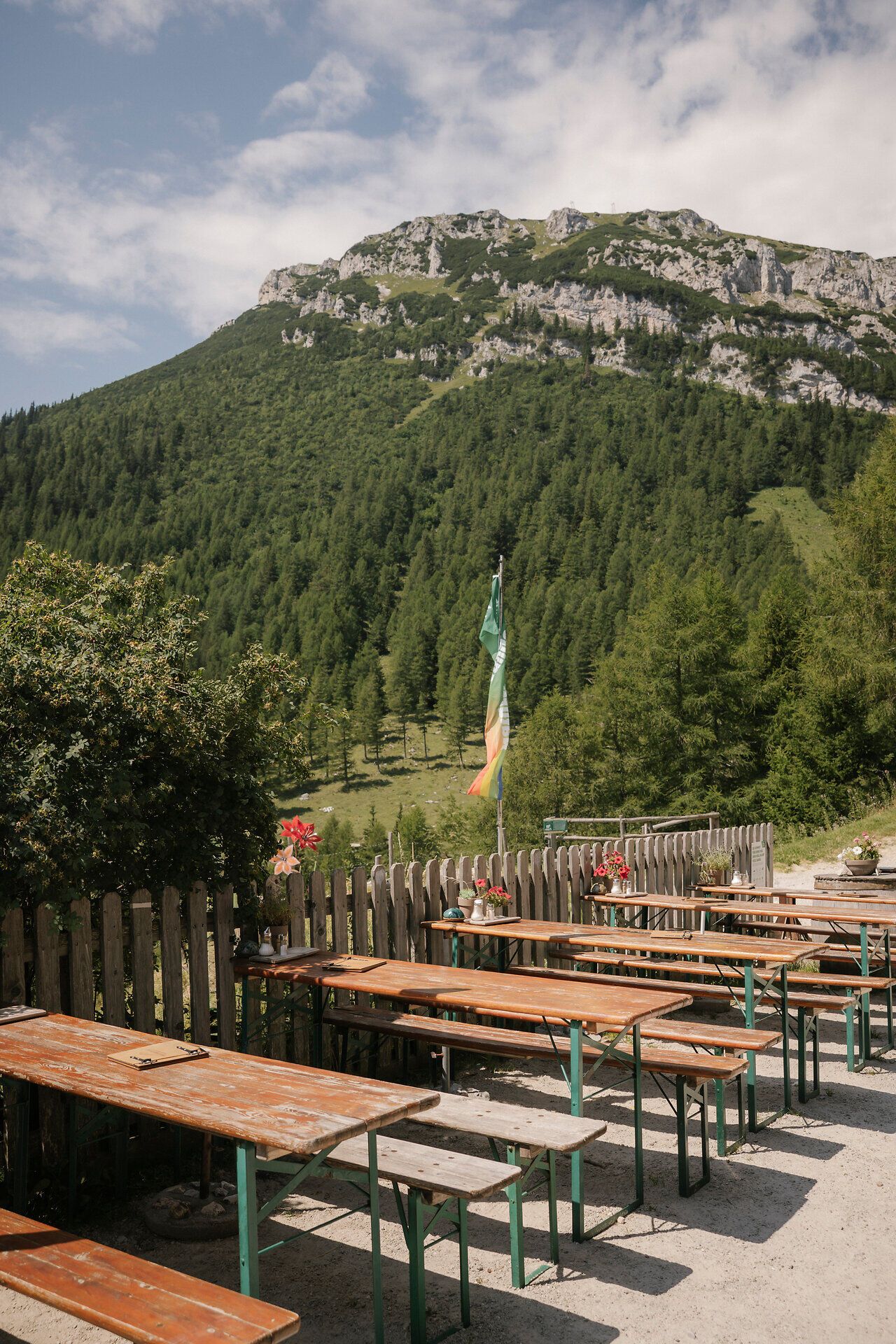 Slnečná terasa v dome Waxriegelhaus na vrchu Rax s drevenými stolmi a výhľadom na okolitú horskú krajinu