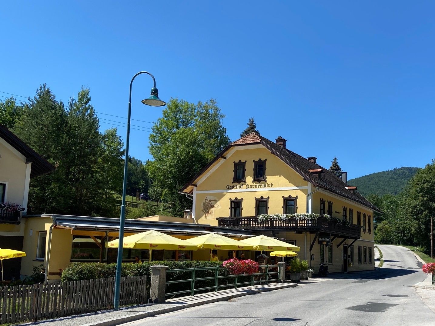 Žltý hostinec s balkónom a slnečníkmi na pozadí modrej oblohy.