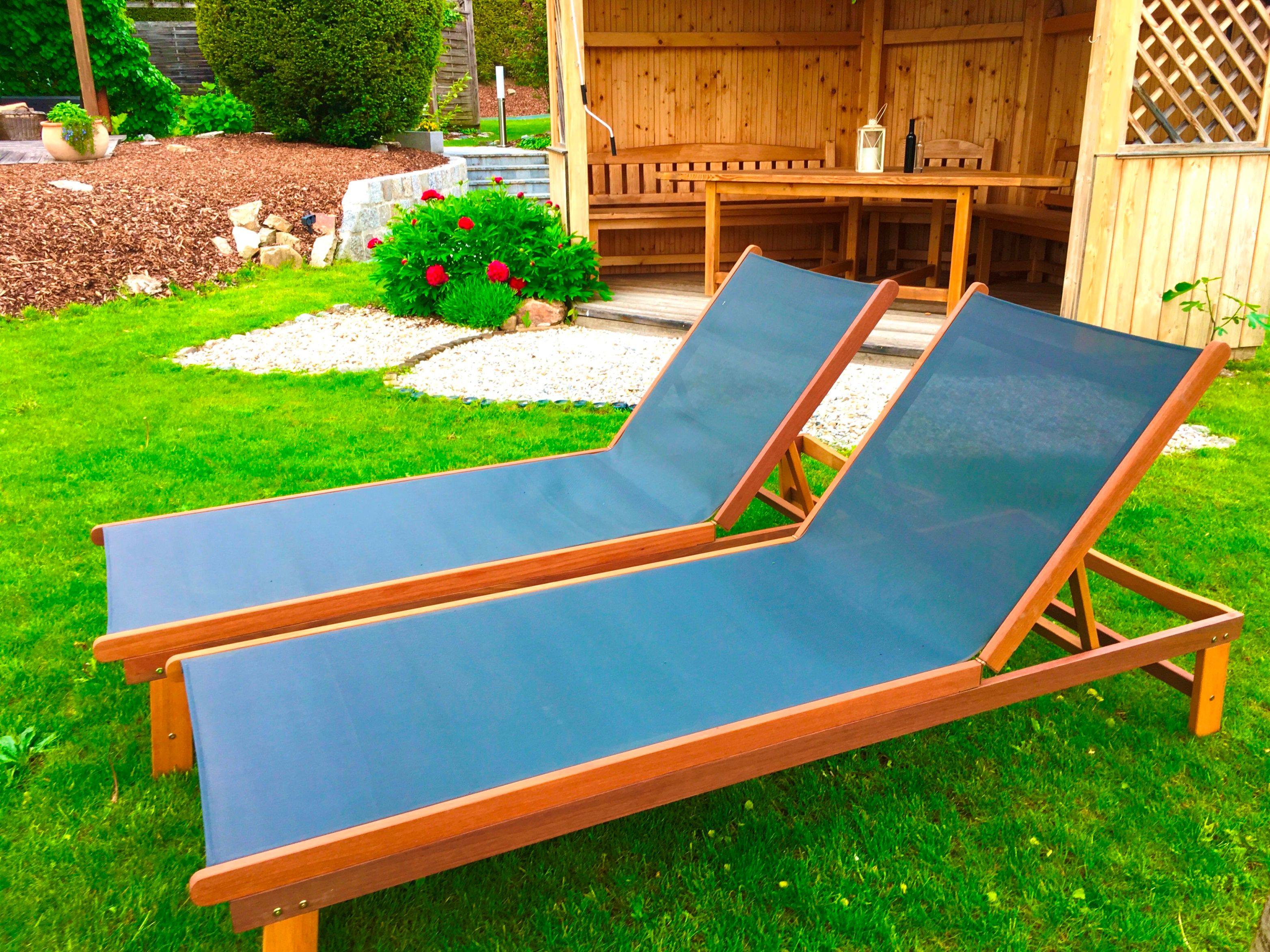 Dve modré ležadlá na zelenom trávniku pred drevenou chatkou v záhrade.