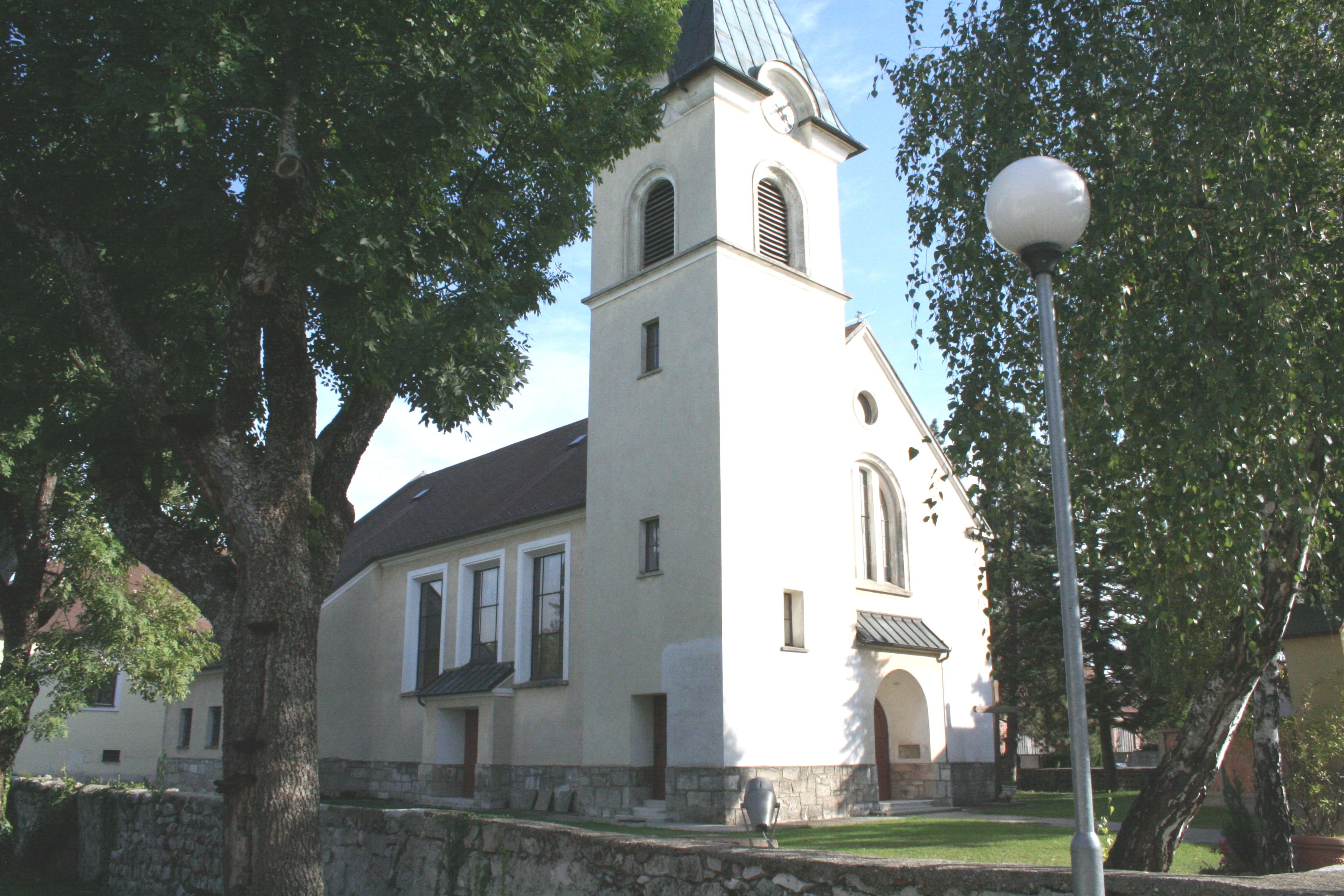 Kostol v Pischelsdorfe s vežou a stromami v popredí.